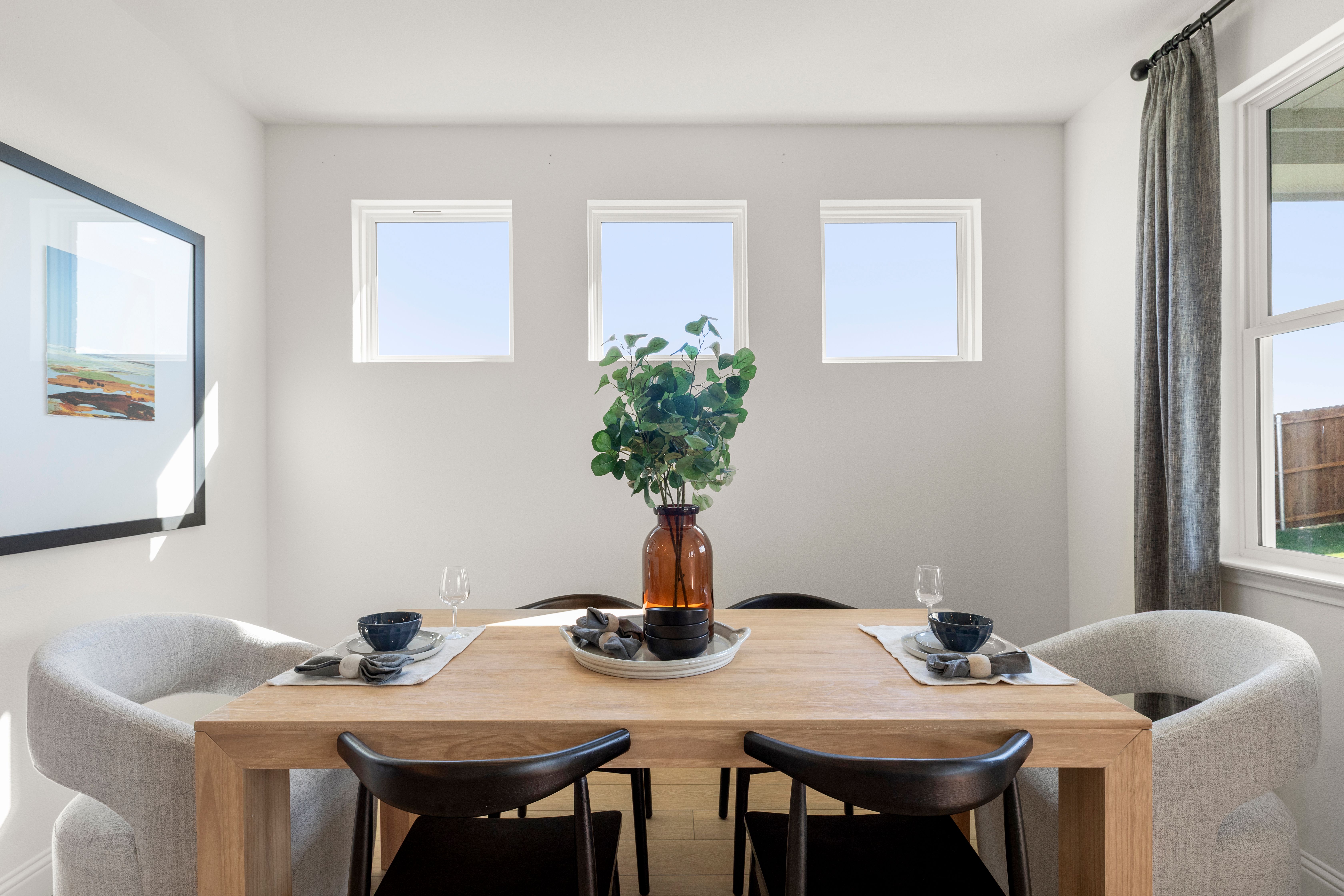 Dining room in The Laurel by Davidson Homes featuring oak table, black chairs, eucalyptus centerpiece, and triple windows with natural light