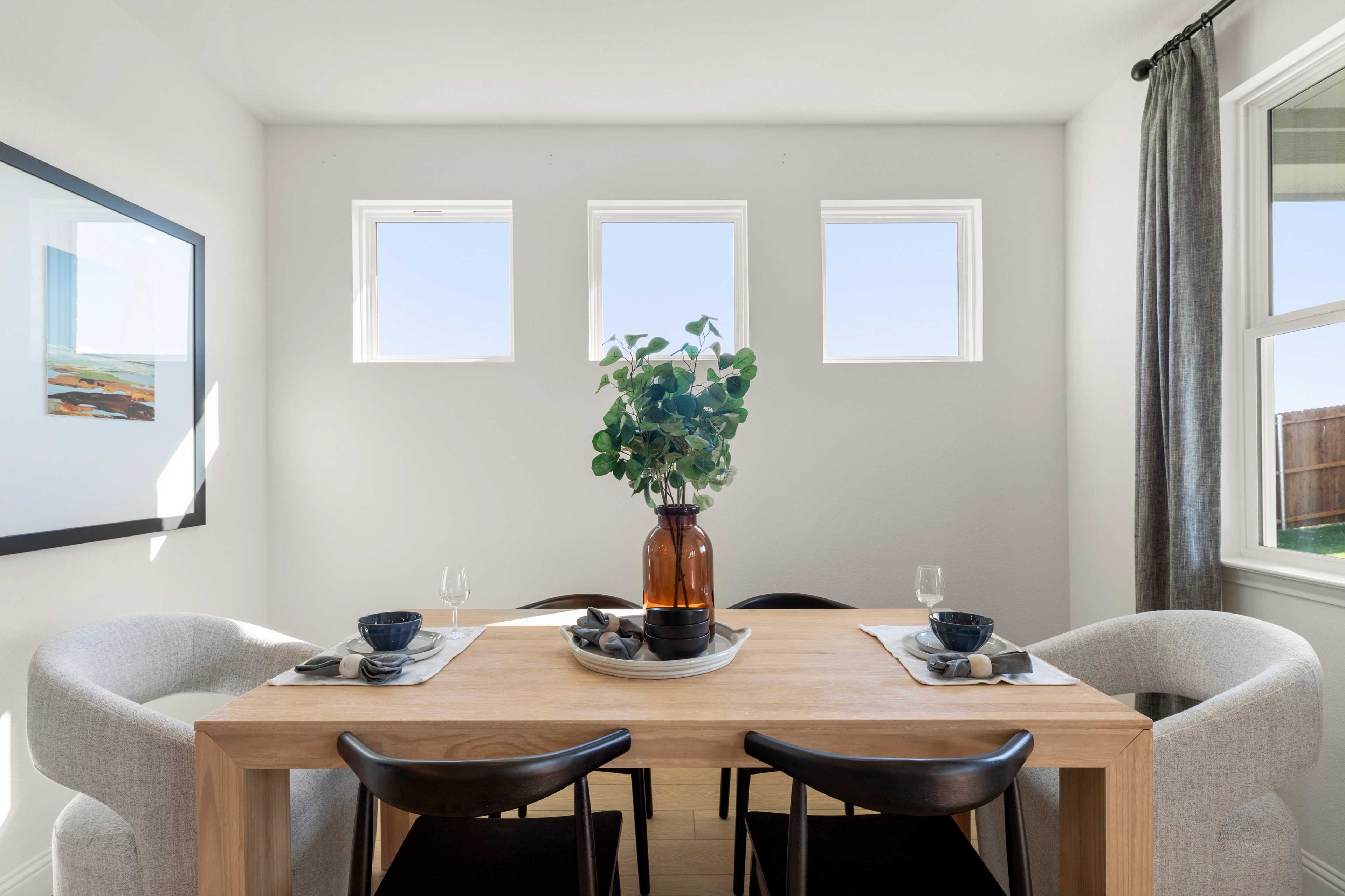Dining room in The Laurel by Davidson Homes featuring oak table, black chairs, eucalyptus centerpiece, and triple windows with natural light