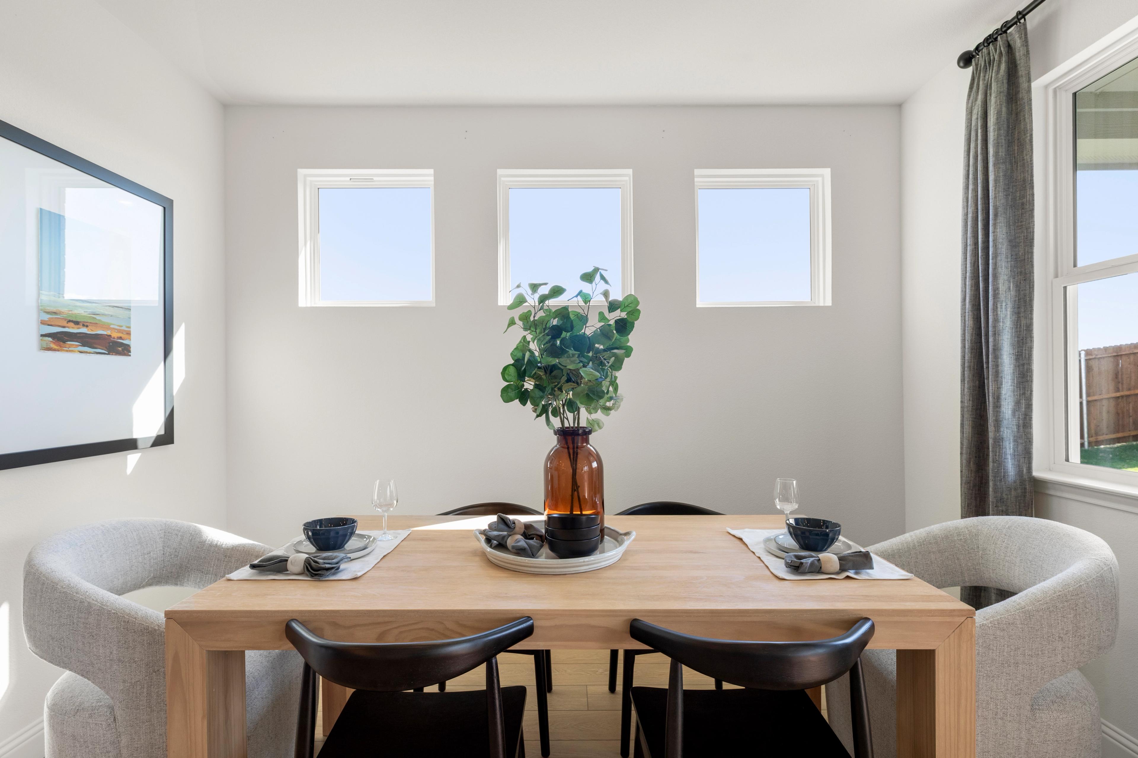 Modern dining room in The Laurel G with oak table, black chairs, gray armchairs, eucalyptus centerpiece, and triple windows with natural light