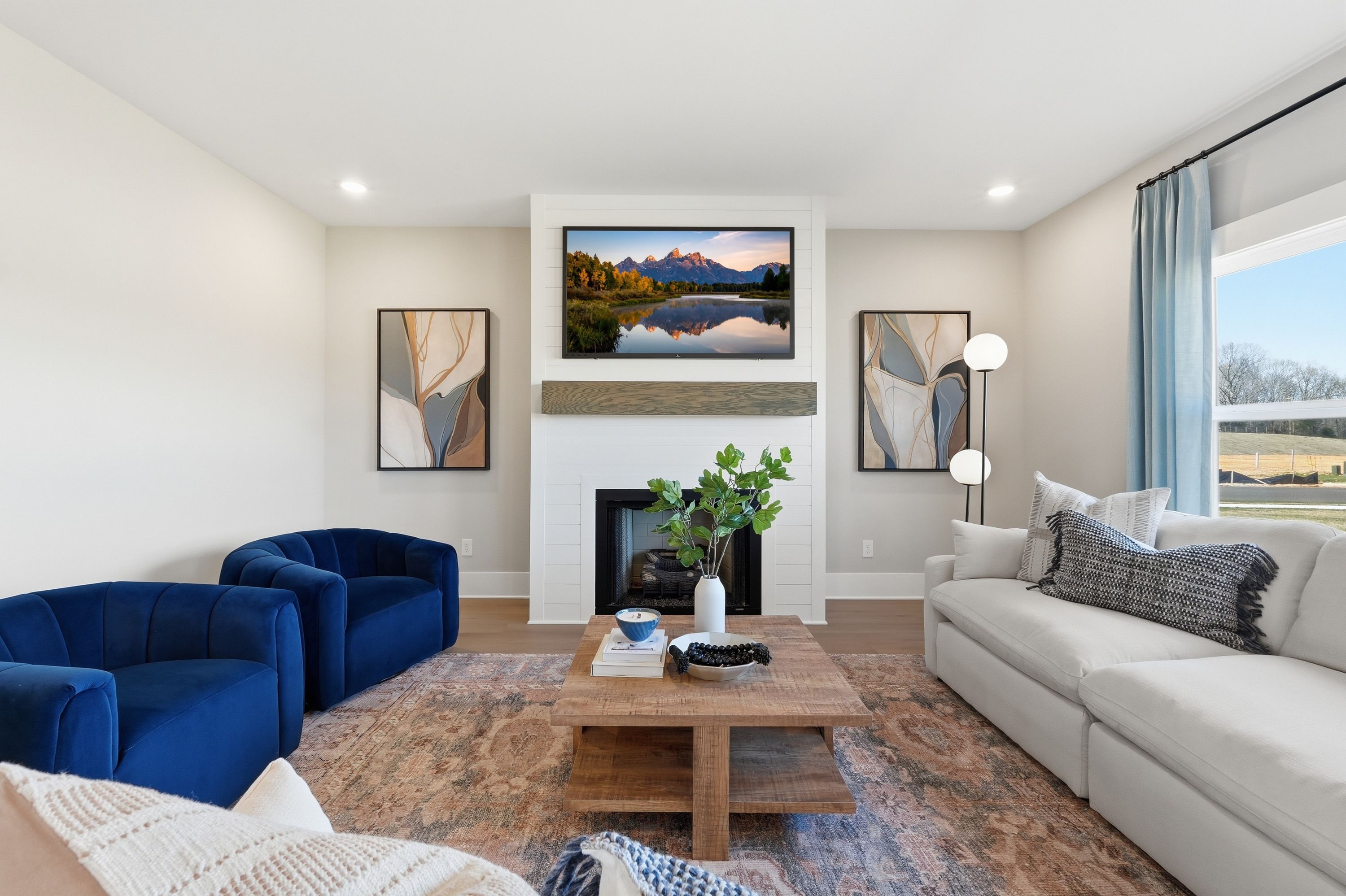 Spacious living room in Berry Cove, New Market AL featuring blue velvet chairs, white sofa, wood coffee table, fireplace and scenic TV art