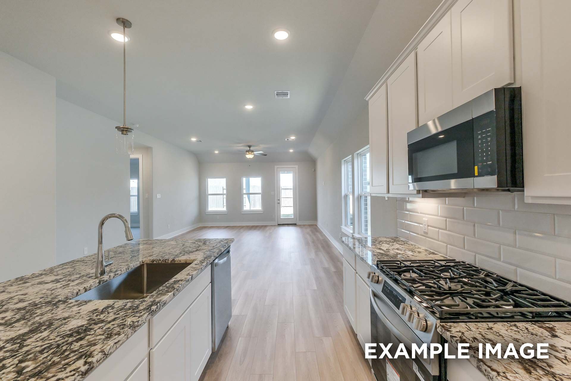 Spacious The Luna K kitchen with white cabinets, granite counters, gas range, subway tile backsplash, open to living area