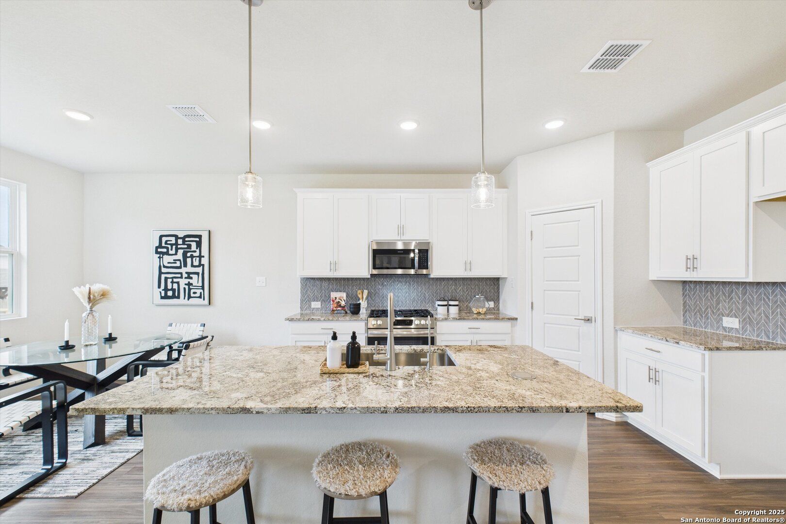 Modern kitchen with white cabinets, swirled granite island, stainless appliances, and pendant lights in The Asheville K, San Antonio