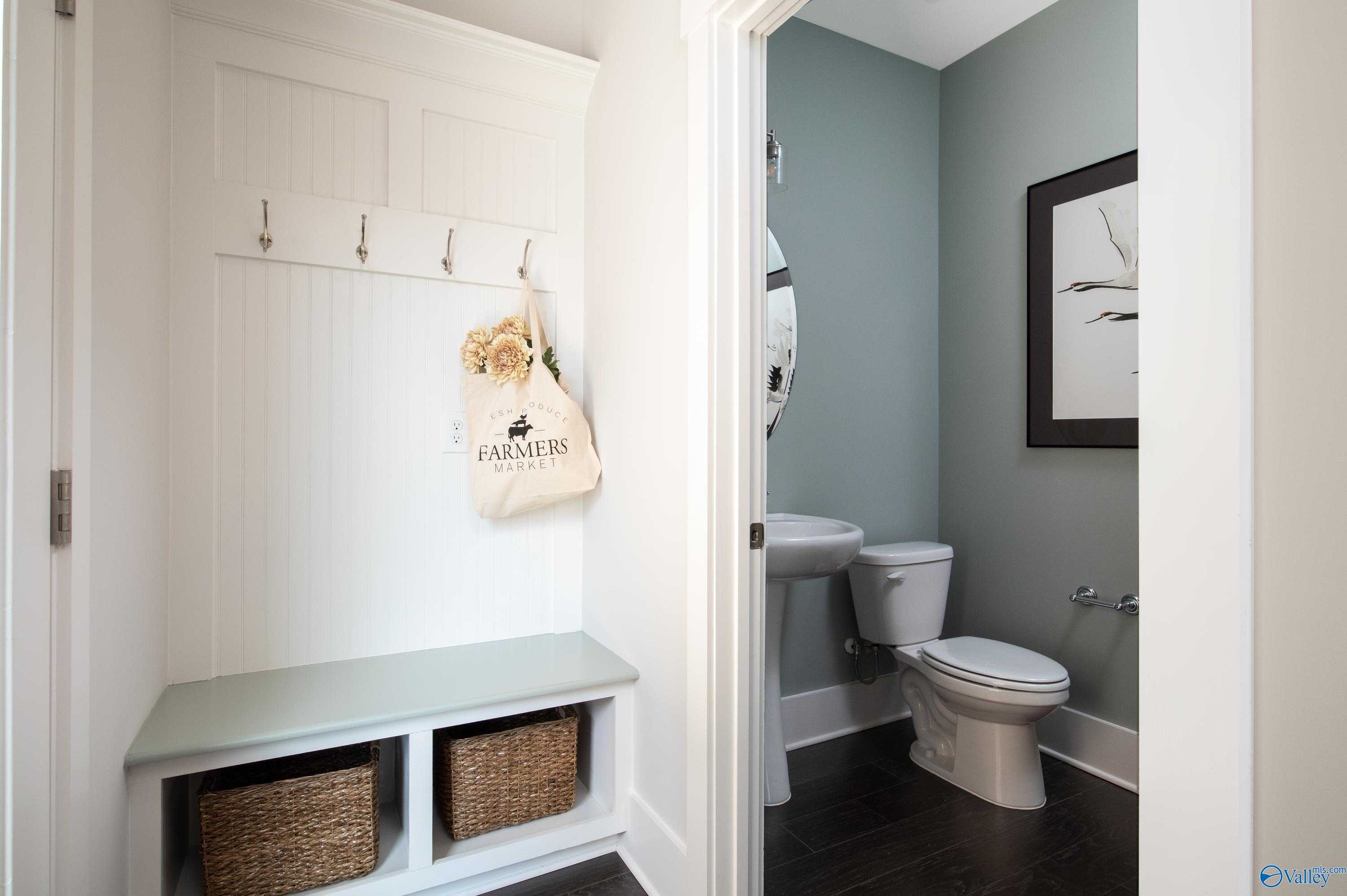 White shiplap mudroom with coat hooks, Farmers tote, bench, and wicker baskets beside light blue powder room in Davidson Homes The Covington C, Decatur AL