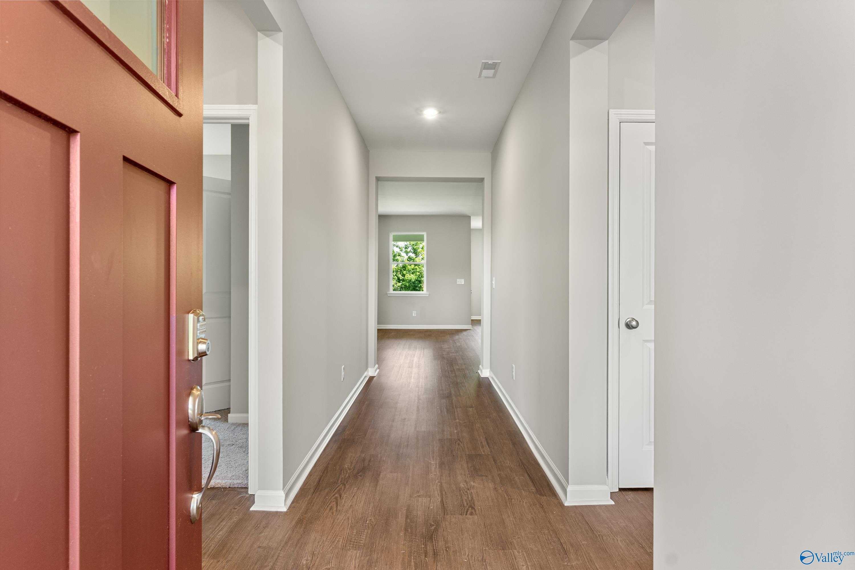 Inviting entryway with red door opening to long hardwood hallway and natural light in Davidson Homes The Sanctuary, Huntsville AL