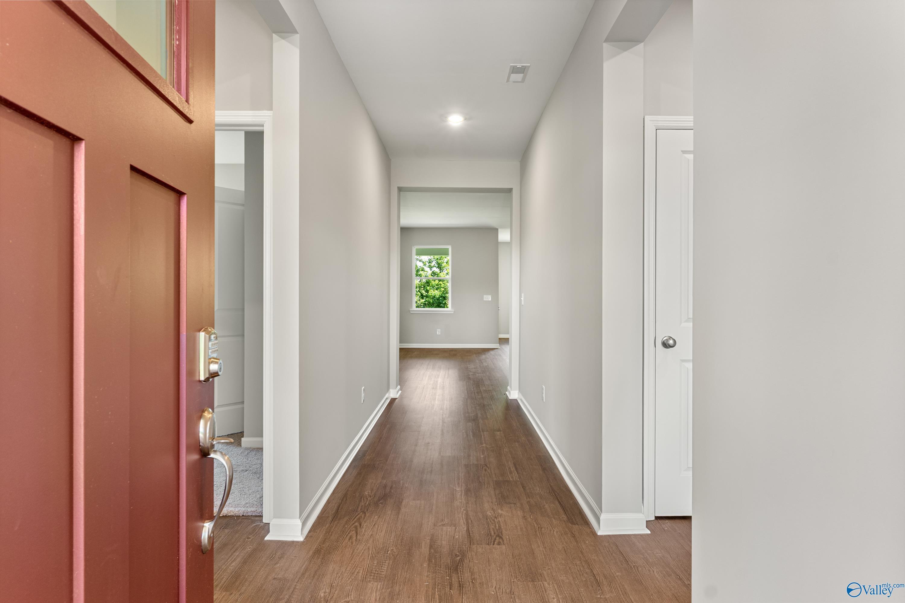 Inviting entryway with red door opening to long hardwood hallway and natural light in Davidson Homes The Sanctuary, Huntsville AL