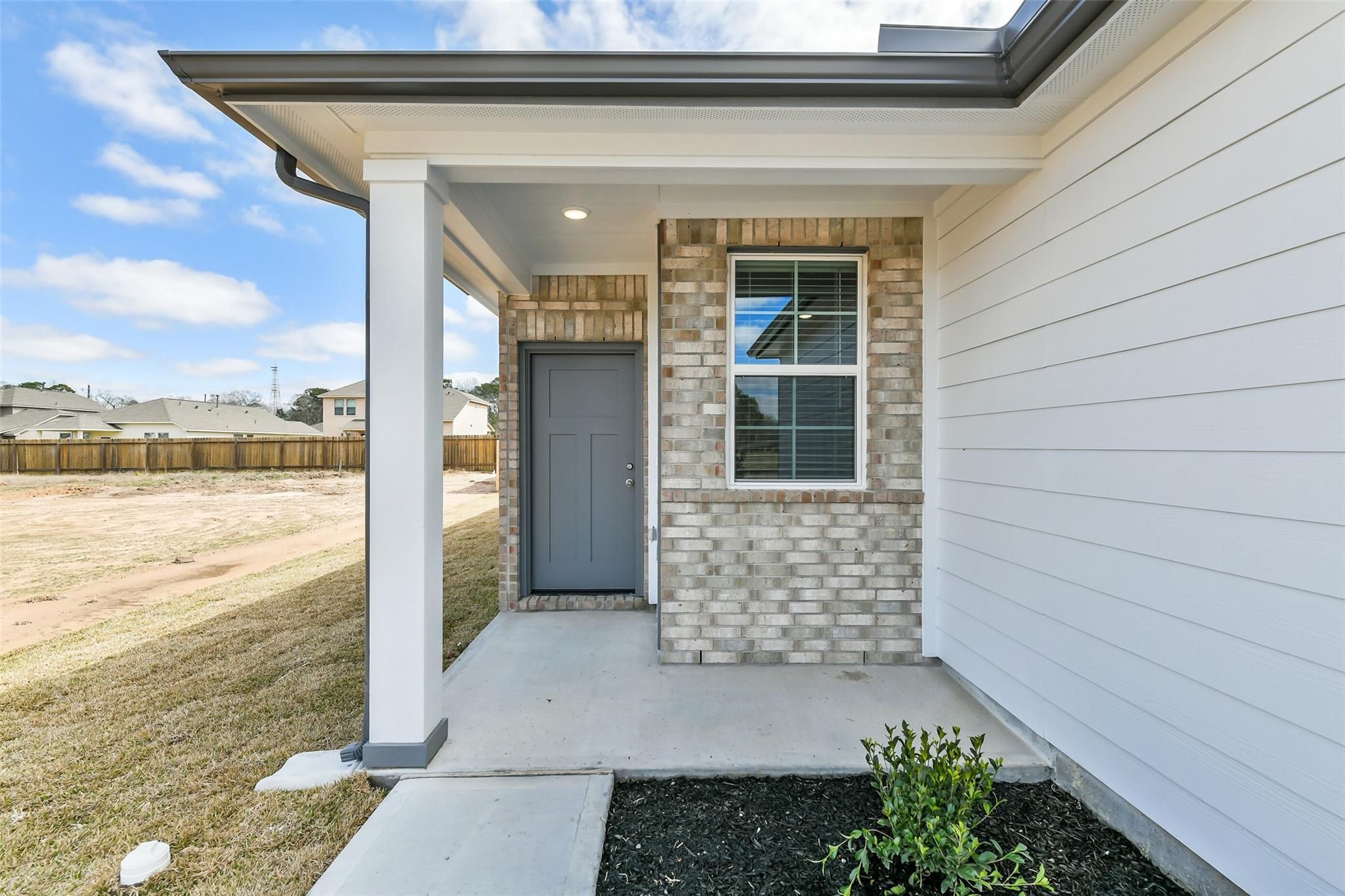 Inviting covered front porch with gray door, brick accents, and white columns on Davidson Homes The Colorado F in Liberty Estates, Cleveland, Texas