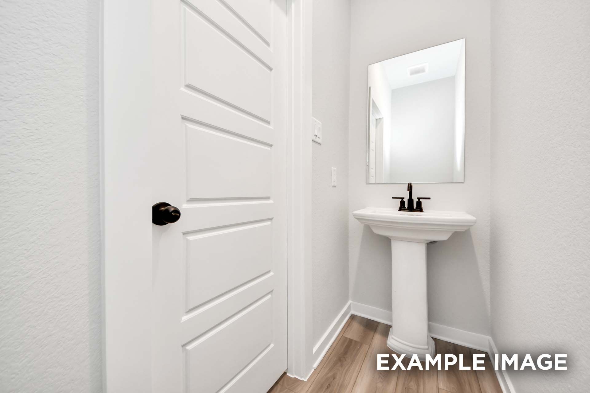 Modern powder room in The Sorrento featuring a white pedestal sink, sleek black faucet, and matching door hardware.