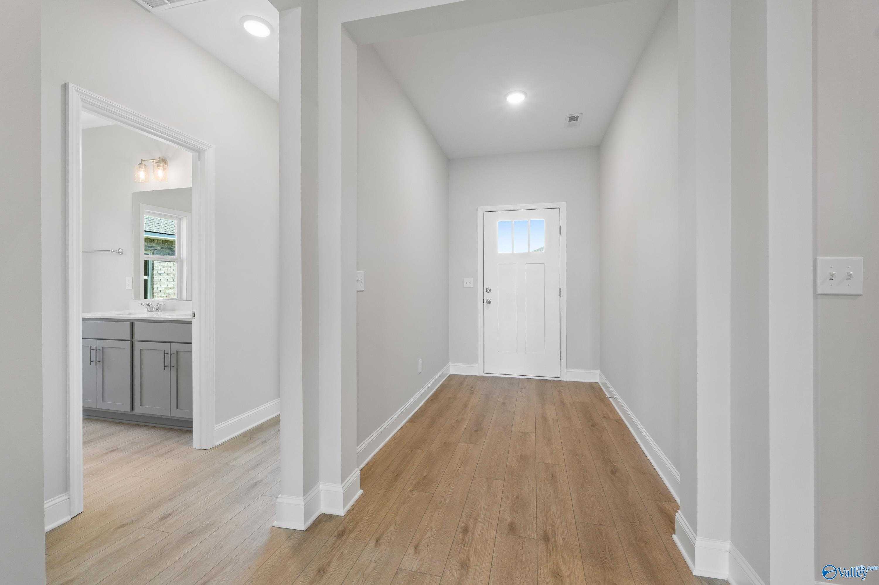 Bright hallway with hardwood floors, white columns, powder room gray vanity, and glass door in Davidson Homes The Everett, Hazel Green, AL