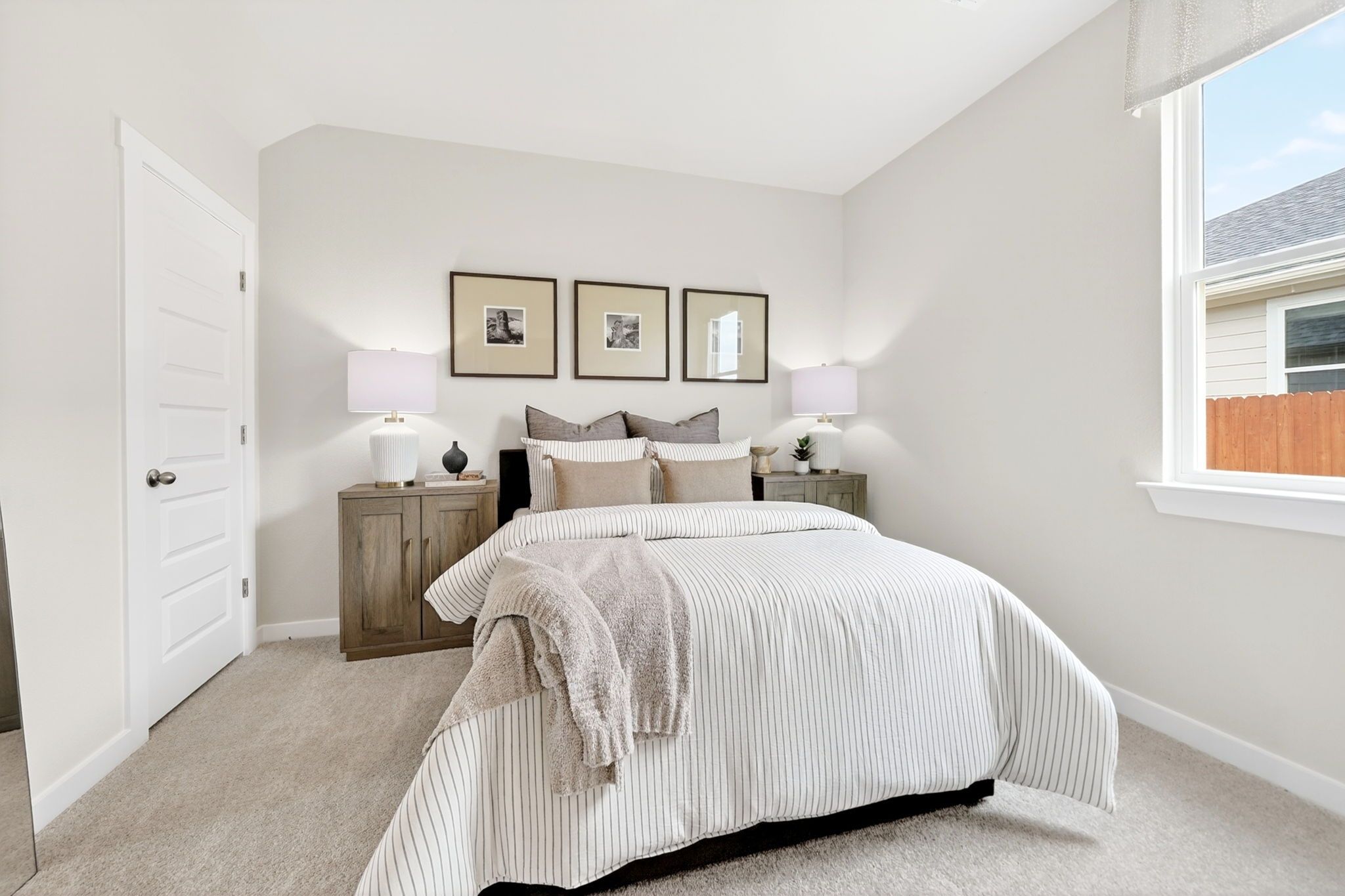 Cozy neutral bedroom in Heartland Texas by Davidson Homes with striped bedding wooden nightstands lamps and window