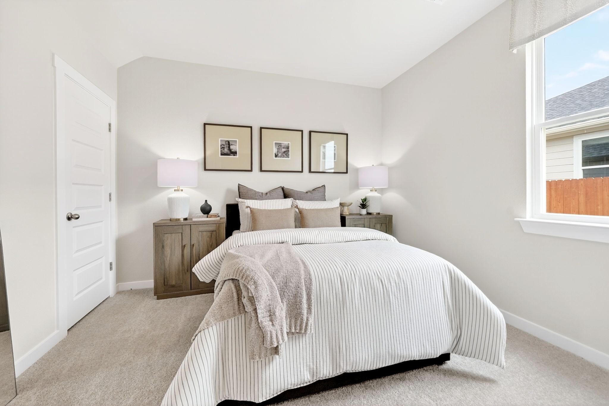Cozy neutral bedroom in Heartland Texas by Davidson Homes with striped bedding wooden nightstands lamps and window