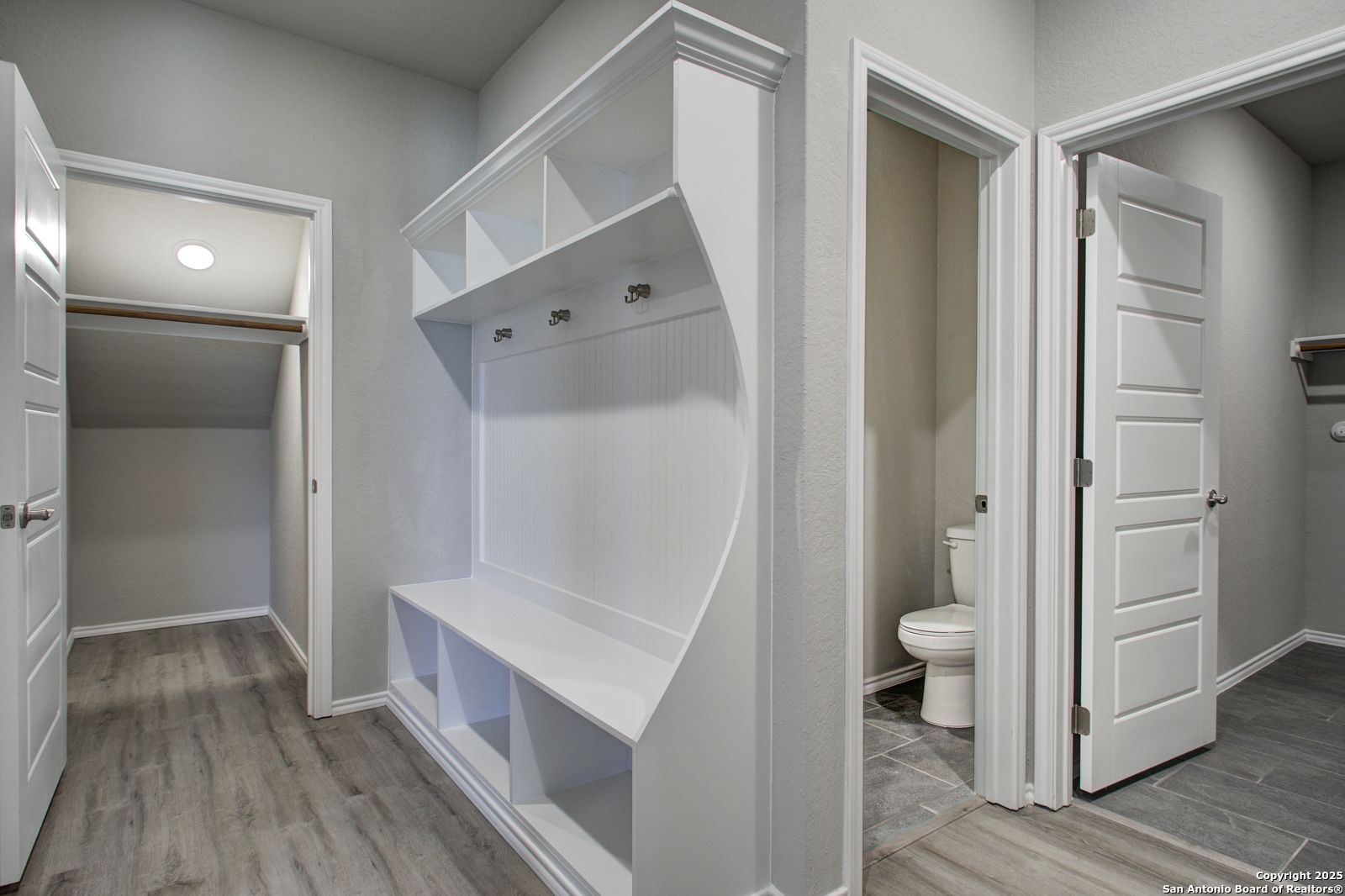 Functional mudroom with white built-in bench, hooks, shelves, and adjacent powder room in Davidson Homes The Douglas G, San Antonio