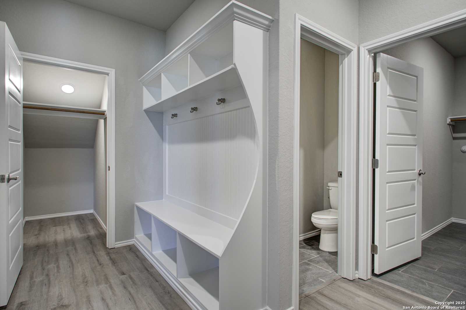 Functional mudroom with white built-in bench, hooks, shelves, and adjacent powder room in Davidson Homes The Douglas G, San Antonio