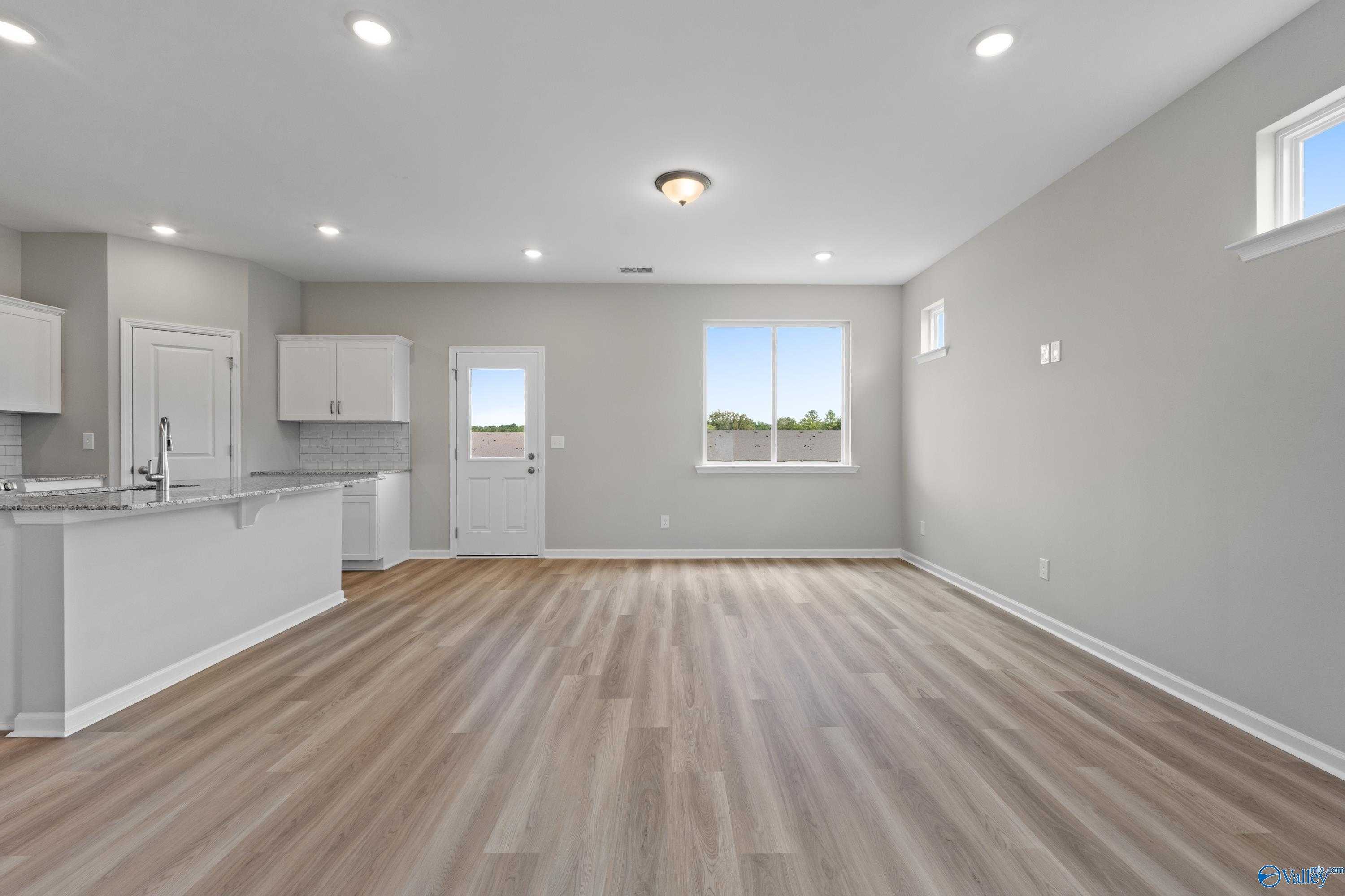 Open kitchen with white island, cabinets, sink, and laminate wood floors in spacious living area of The Augusta floor plan, Madison, Alabama