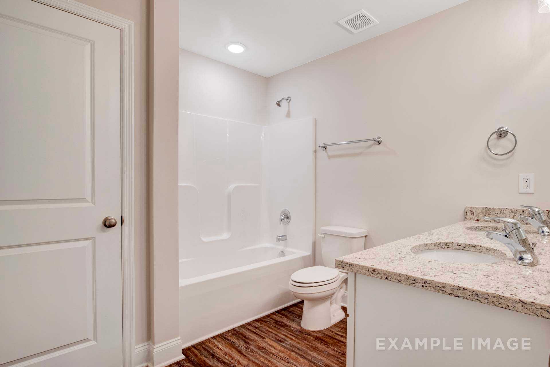 Spacious upstairs bathroom in The Charleston featuring white tub, granite vanity, toilet, and hardwood floors by Davidson Homes