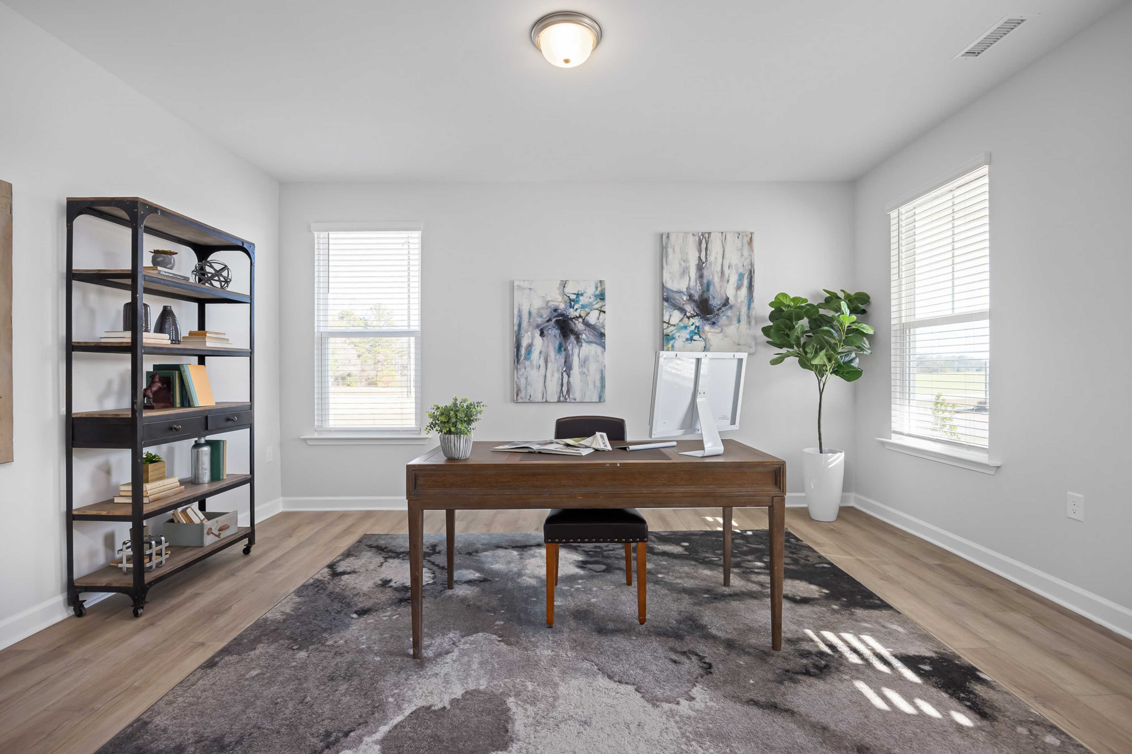 Modern home office at Stagecoach Corner in Mebane NC with wooden desk, metal bookshelf, fiddle leaf fig plant, and abstract wall art