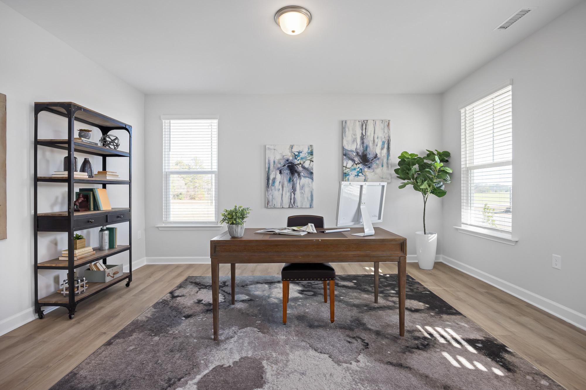 Modern home office at Stagecoach Corner in Mebane NC with wooden desk, metal bookshelf, fiddle leaf fig plant, and abstract wall art