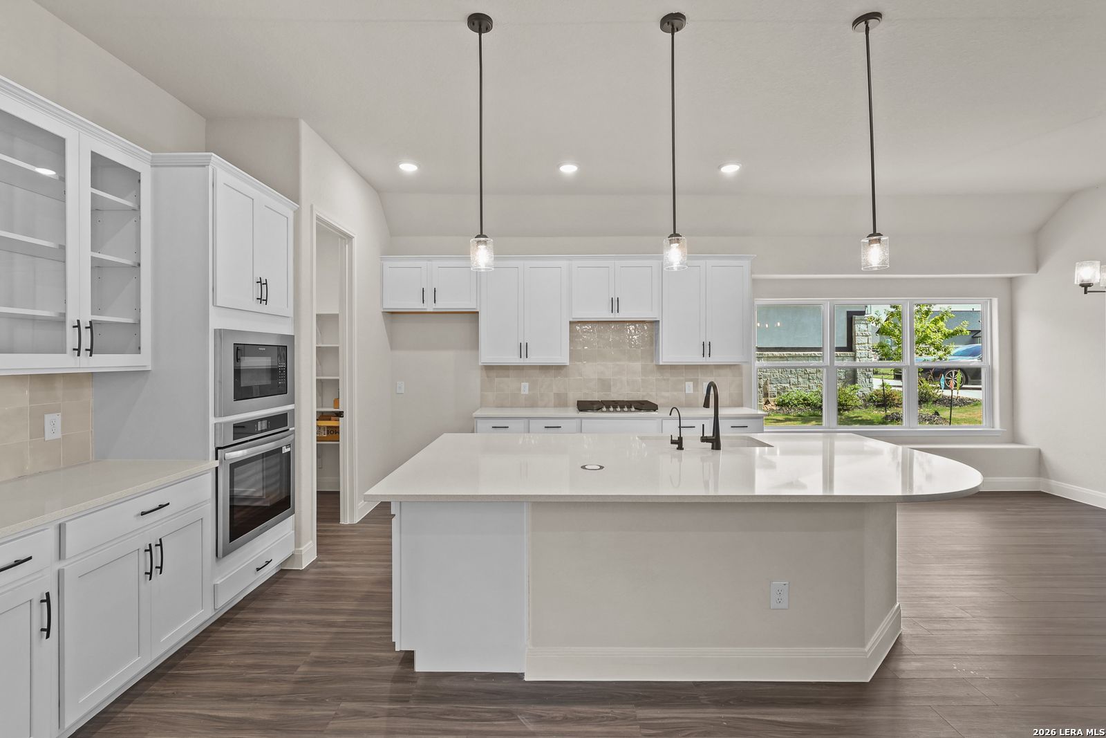 Modern white kitchen with large island and stainless appliances in The Summerlin B home at Potranco Oaks, Castroville, TX.
