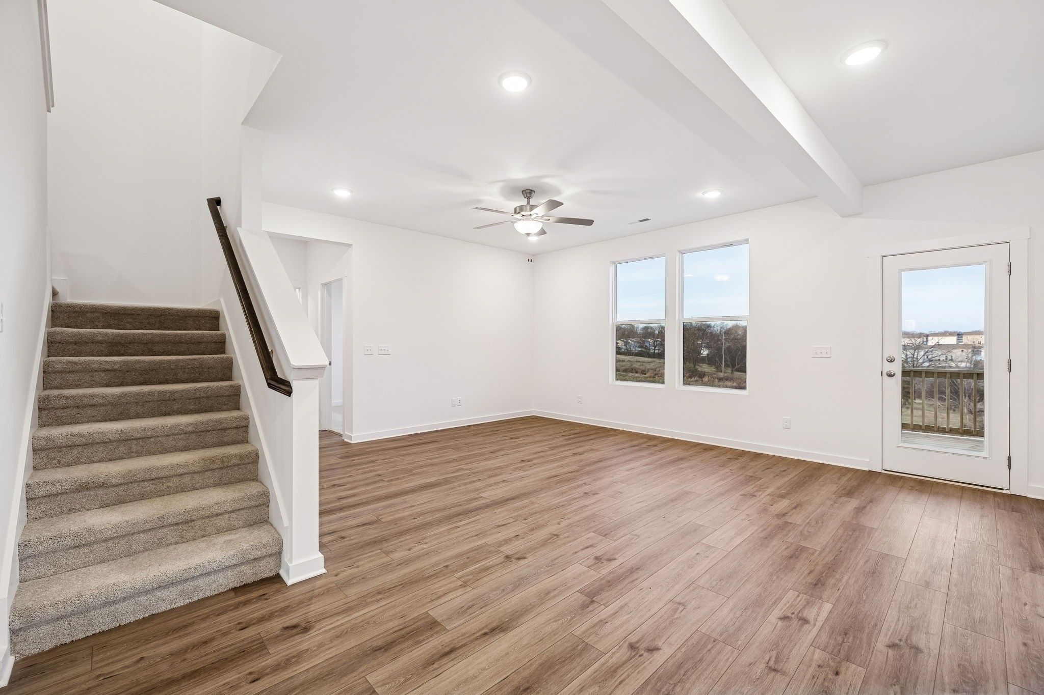 Spacious open living room with hardwood floors, carpeted staircase, ceiling fan, and large windows to countryside in The Willow home, Calista Farms