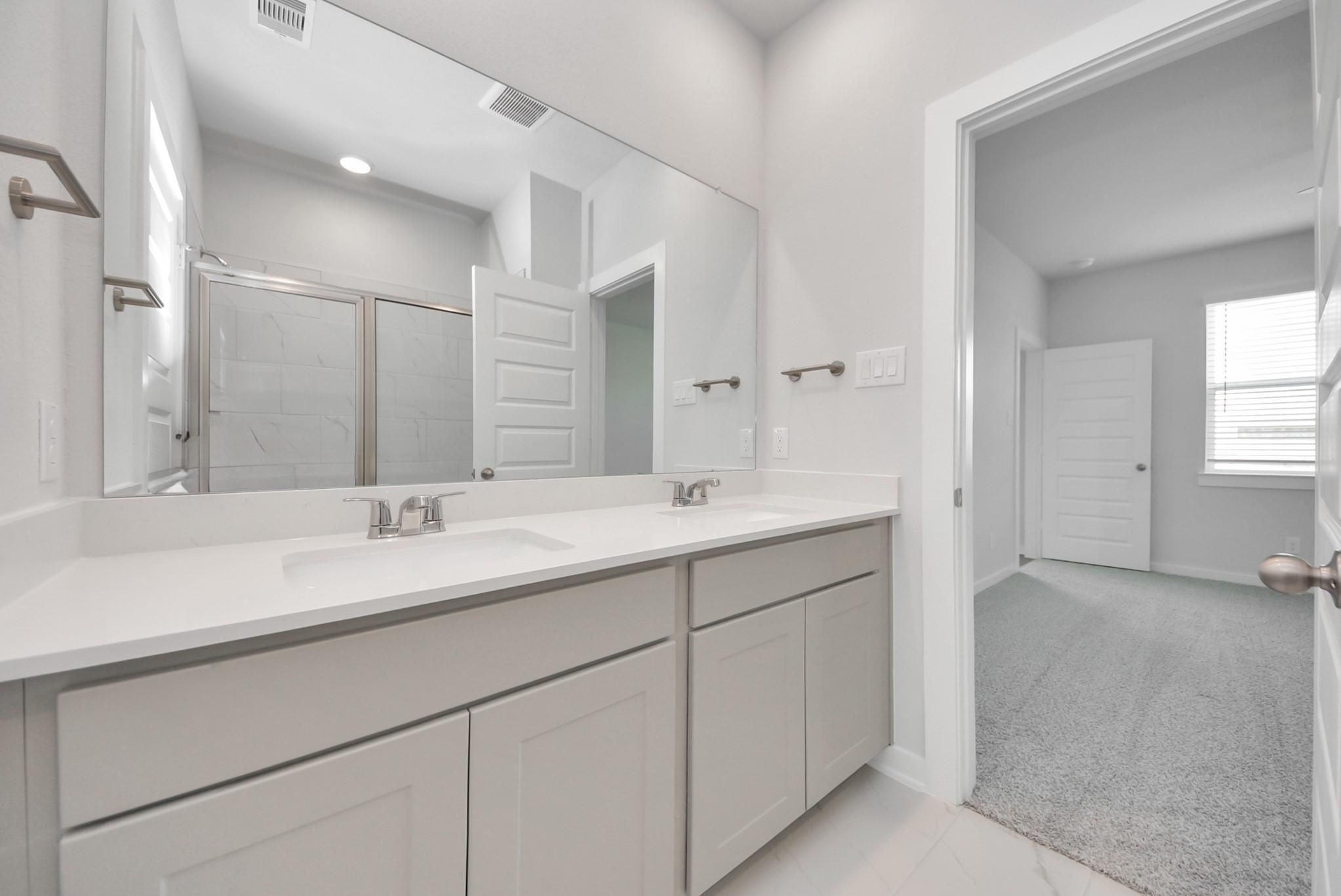 Dual-sink bathroom vanity with large mirror in Davidson Homes The San Marcos E floor plan at Emberly, Beasley, Texas