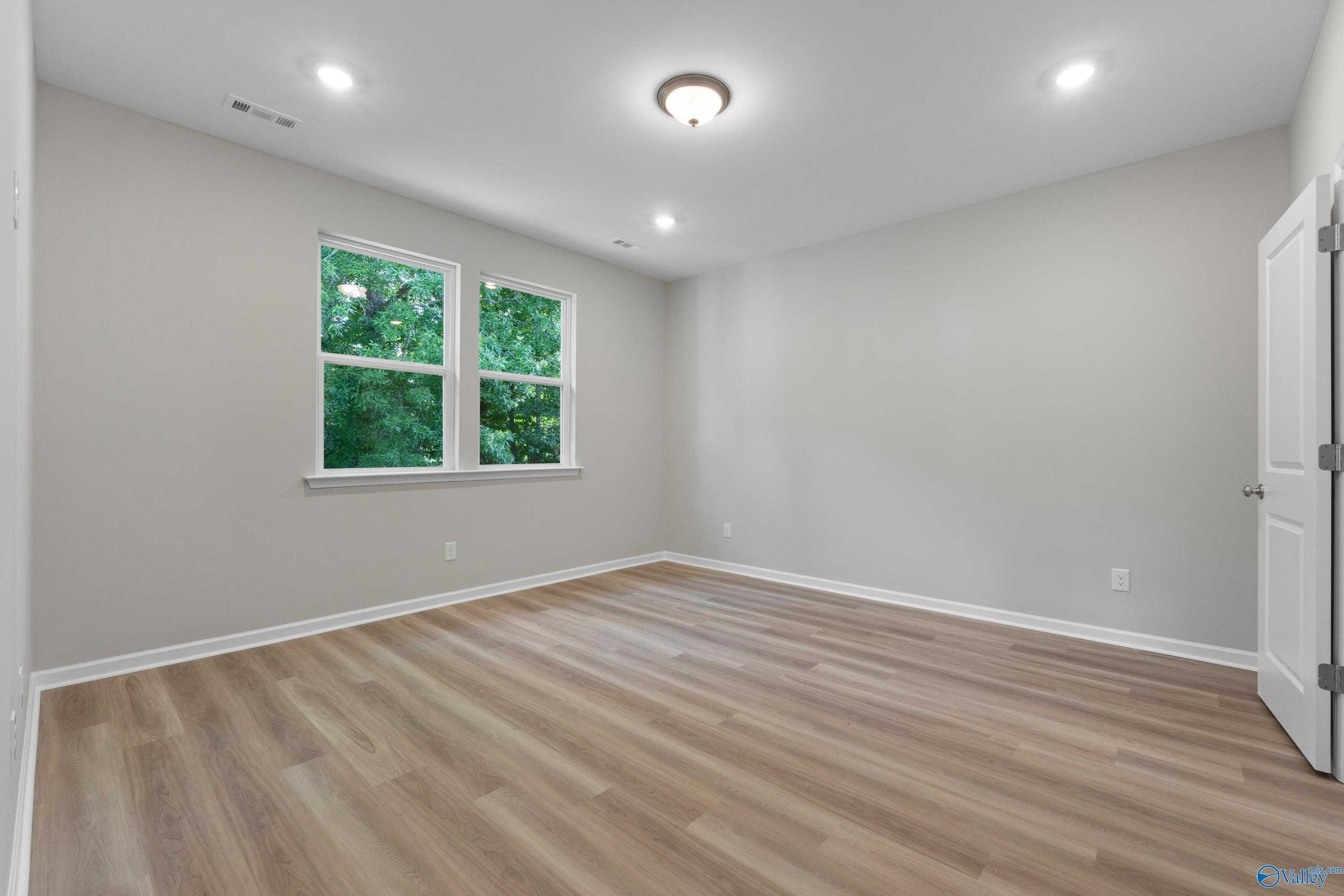 Bright bedroom with large windows overlooking greenery, hardwood floors, and neutral walls in Davidson Homes The Polaris, Fayetteville, TN
