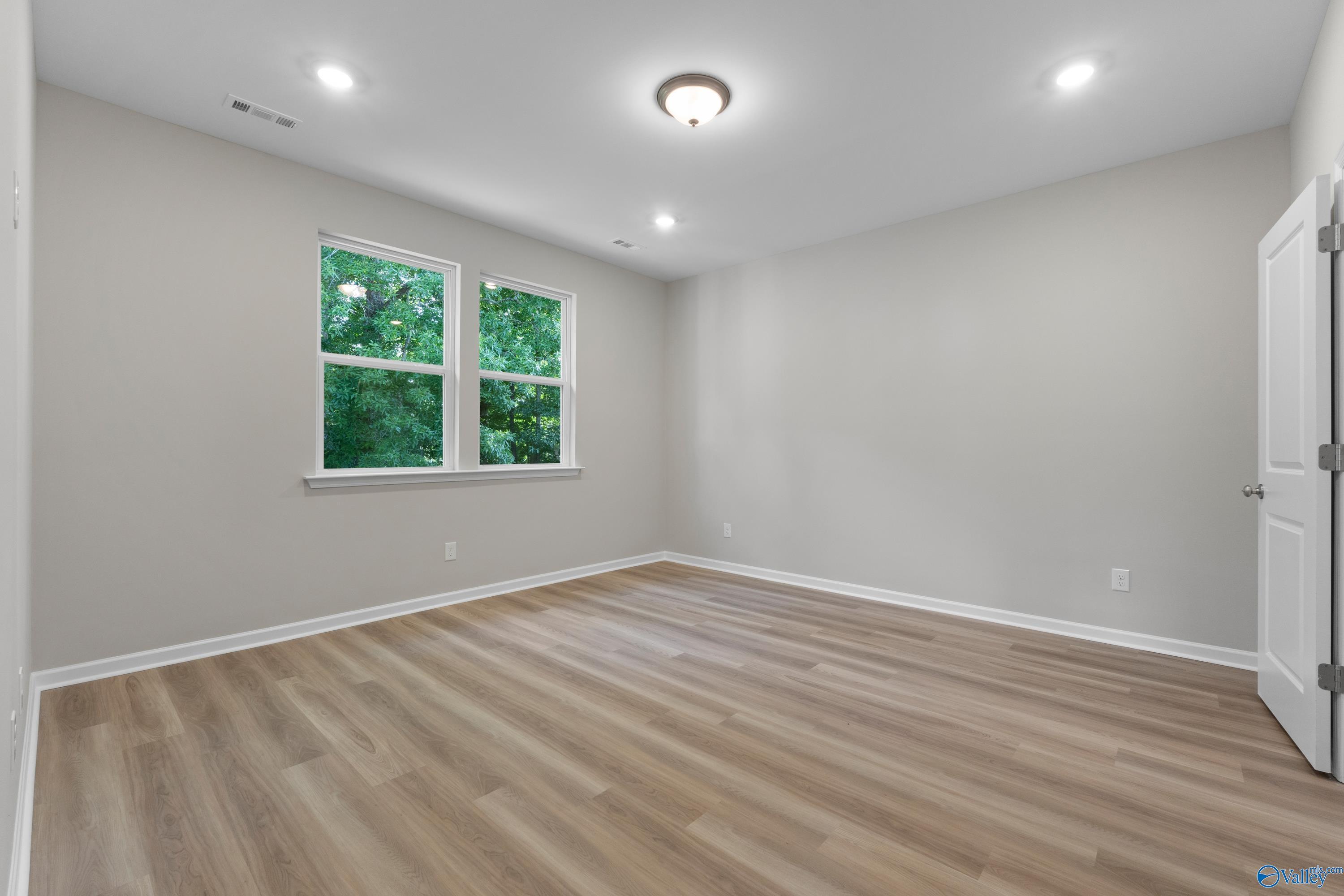 Bright bedroom with gray walls, large green-view windows, and hardwood floors in Davidson Homes The Polaris, Fayetteville, TN