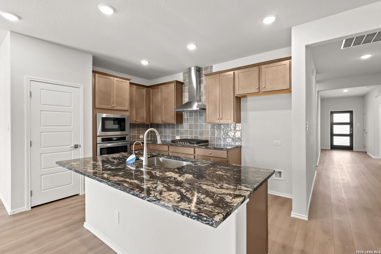 Modern kitchen with granite island, stainless appliances, wood cabinets, and tile backsplash in The Daphne I floor plan, Bricewood San Antonio