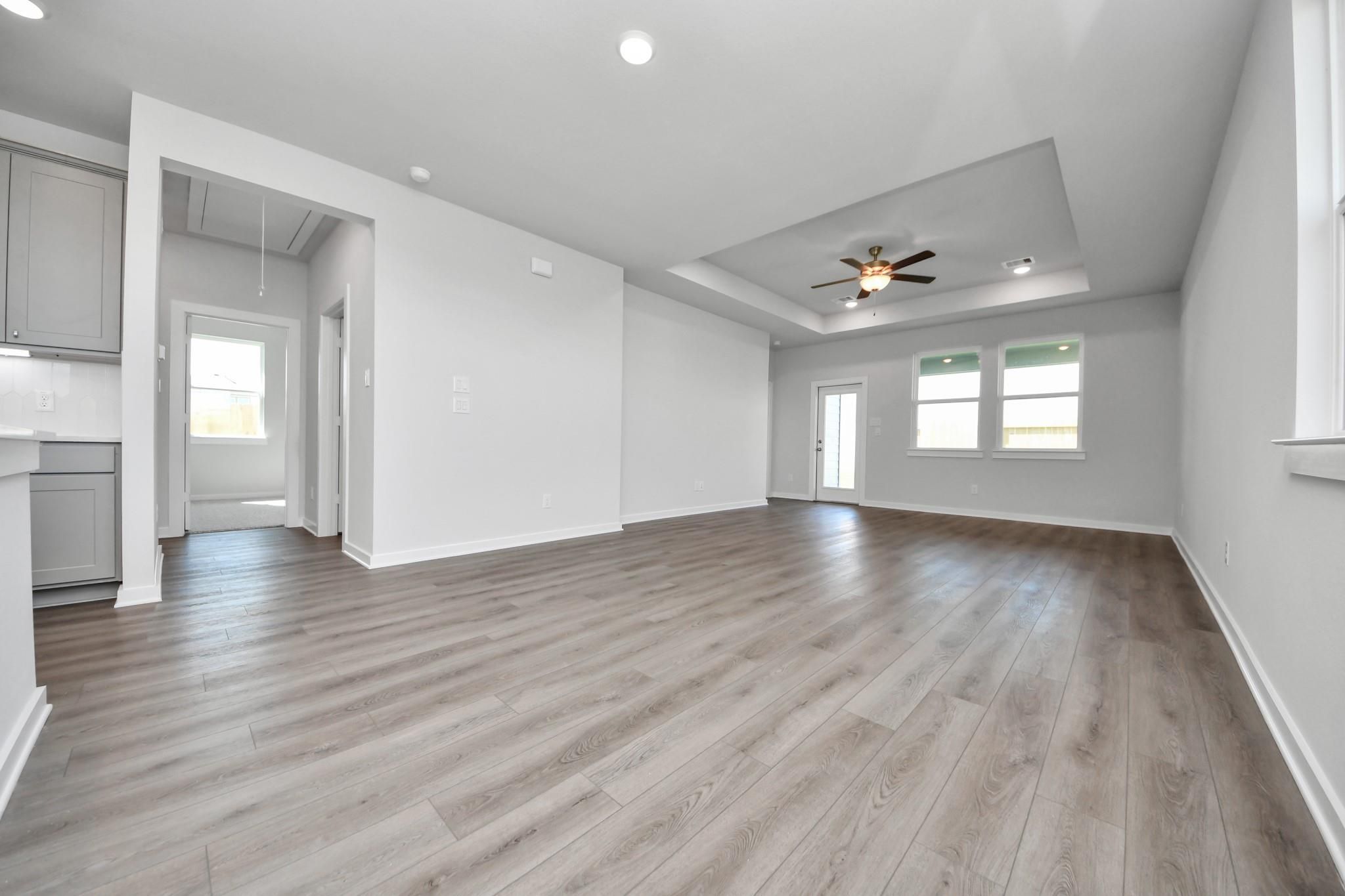 Open-concept living room with tray ceiling and wood-style flooring in The Riviera A floor plan at Emberly, Beasley, TX.