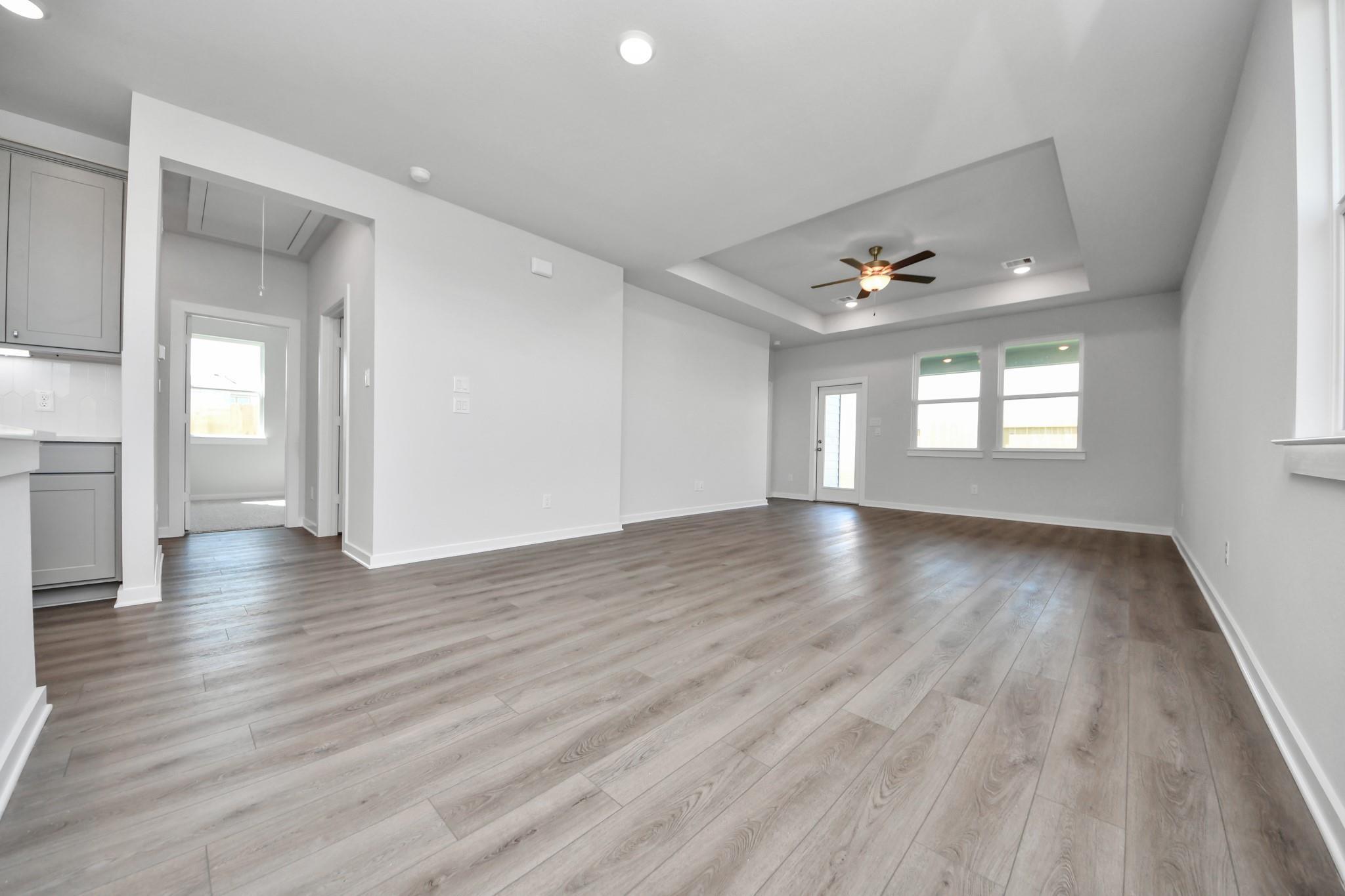 Open-concept living room with tray ceiling and wood-style flooring in The Riviera A floor plan at Emberly, Beasley, TX.