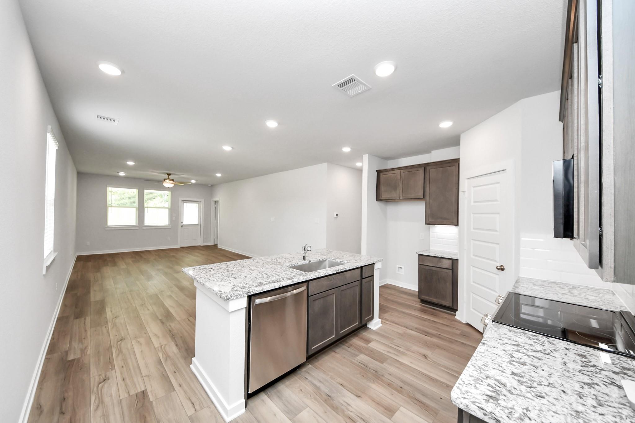 Open-concept kitchen with granite island and wood-style flooring in The Sabine E floor plan, Liberty Estates, Cleveland, TX.