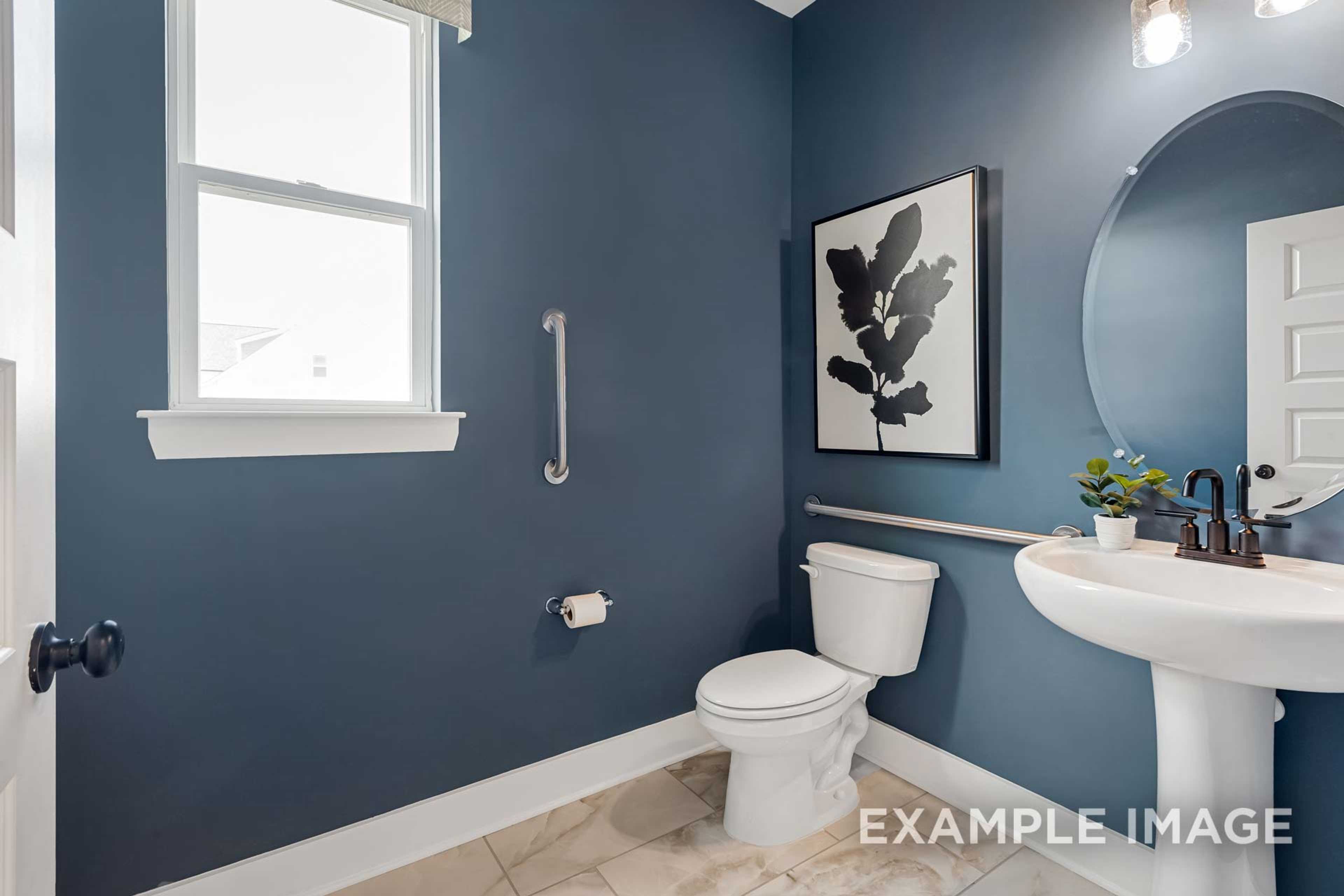Navy blue powder room in The Ridgeport B with pedestal sink, round mirror, leaf artwork, and accessibility grab bars