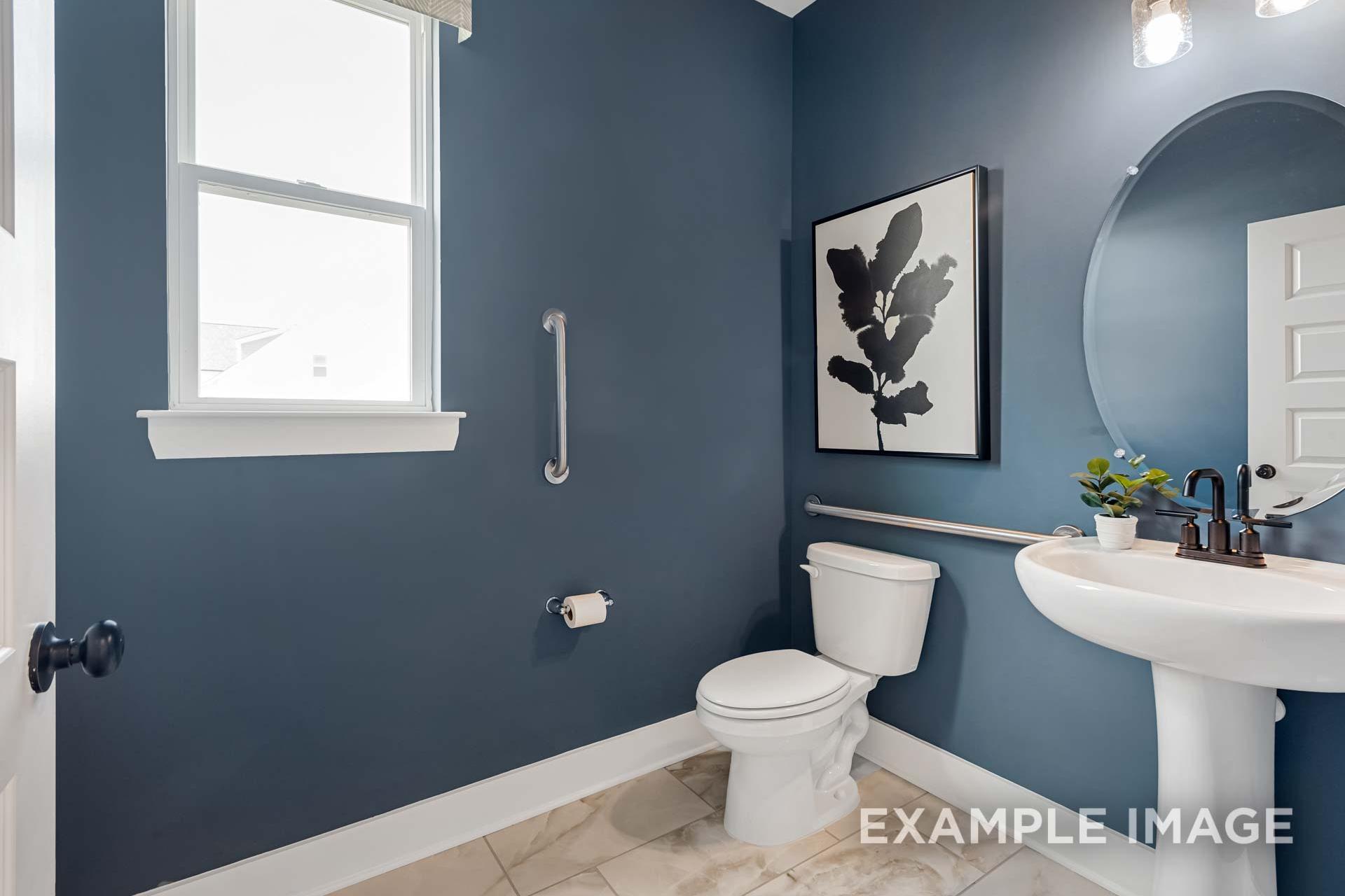 Navy blue powder room in The Ridgeport B with pedestal sink, round mirror, leaf artwork, and accessibility grab bars