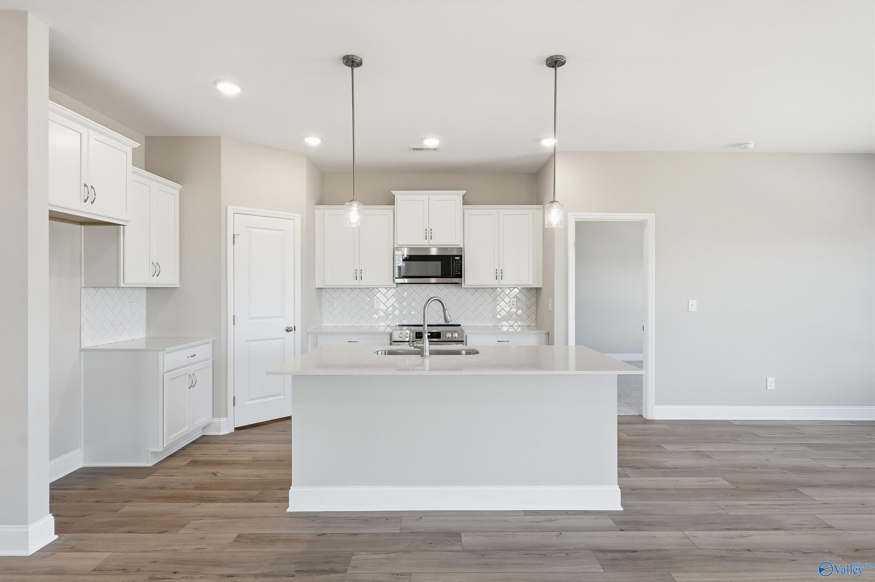 Modern kitchen featuring white shaker cabinets, gray island with sink, stainless microwave, and hardwood floors in The Franklin C, New Market, AL