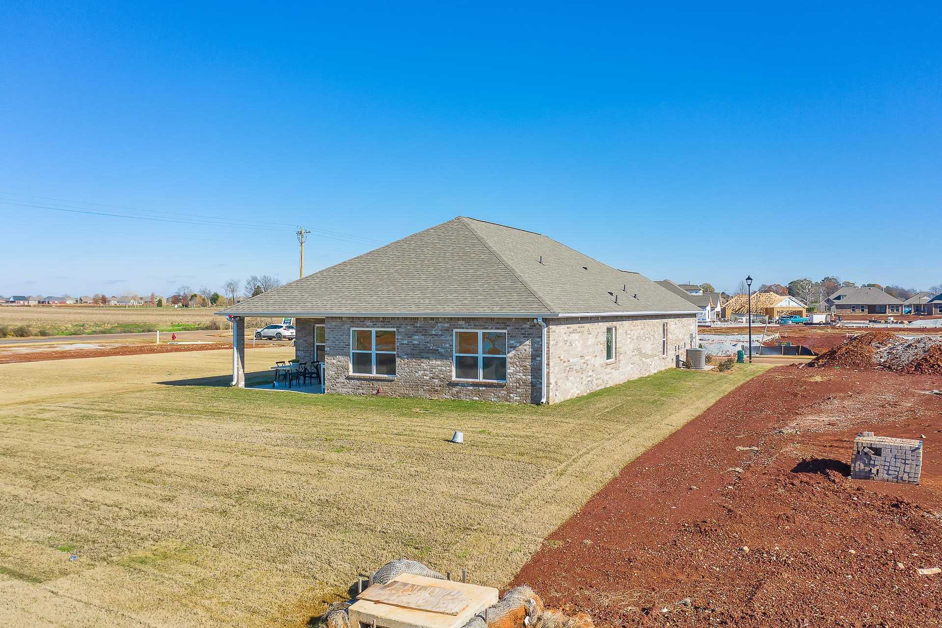 Brick home exterior at Newby Chapel in Athens Alabama with covered porch, gray roof, and surrounding construction site