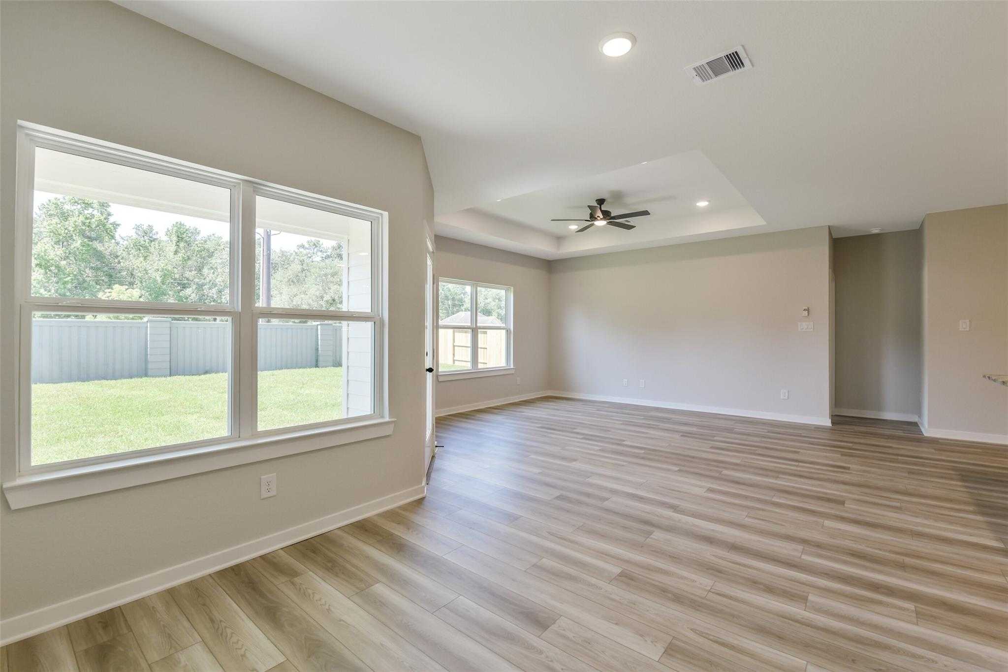 Bright living room with hardwood floors, ceiling fan, and large windows overlooking grassy backyard in 4-bedroom Davidson Homes The Daphne H, Crosby TX