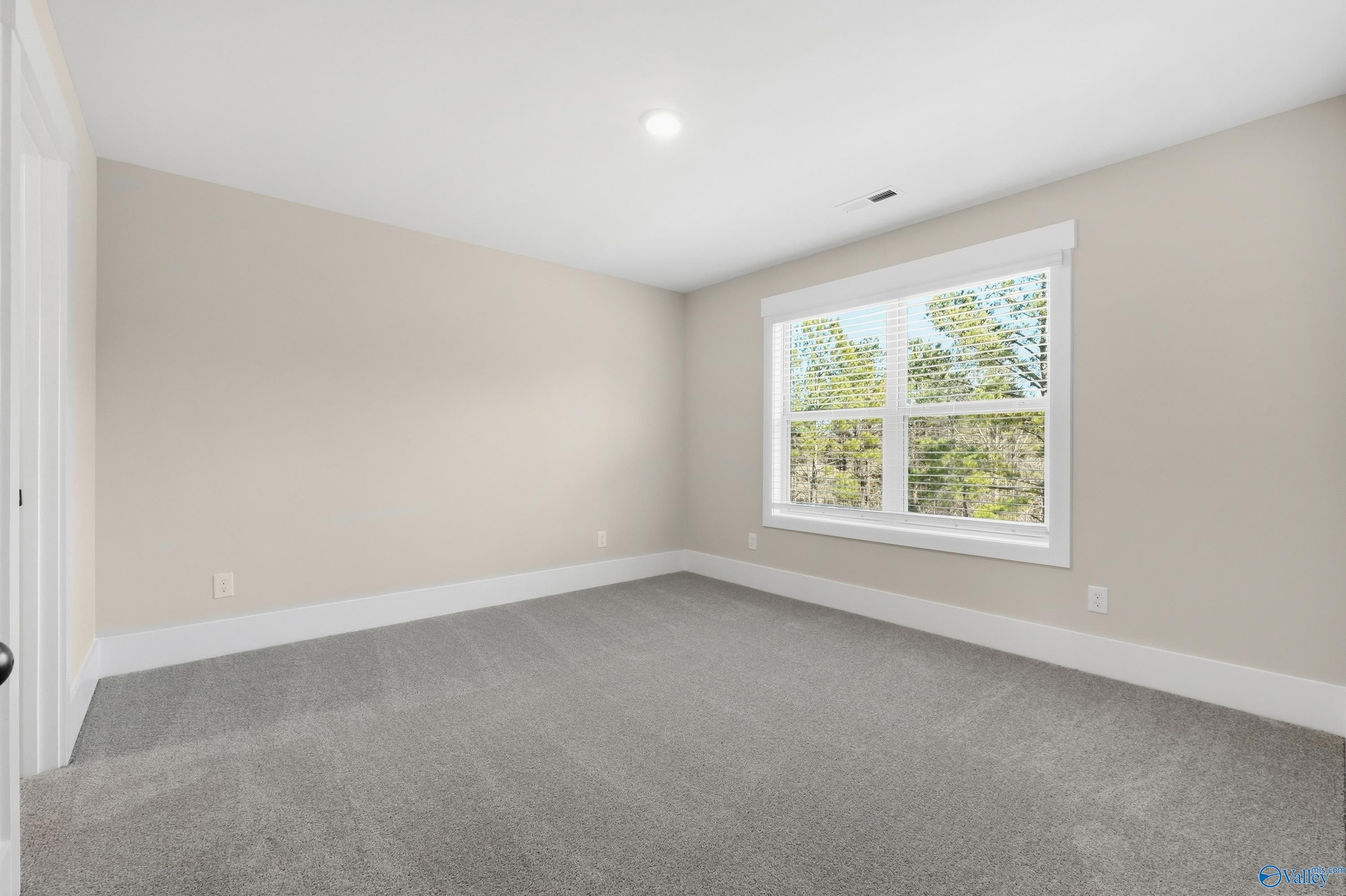 Bright secondary bedroom with beige walls, large window overlooking trees, gray carpet in Davidson Homes The Shelby A, Athens, Alabama