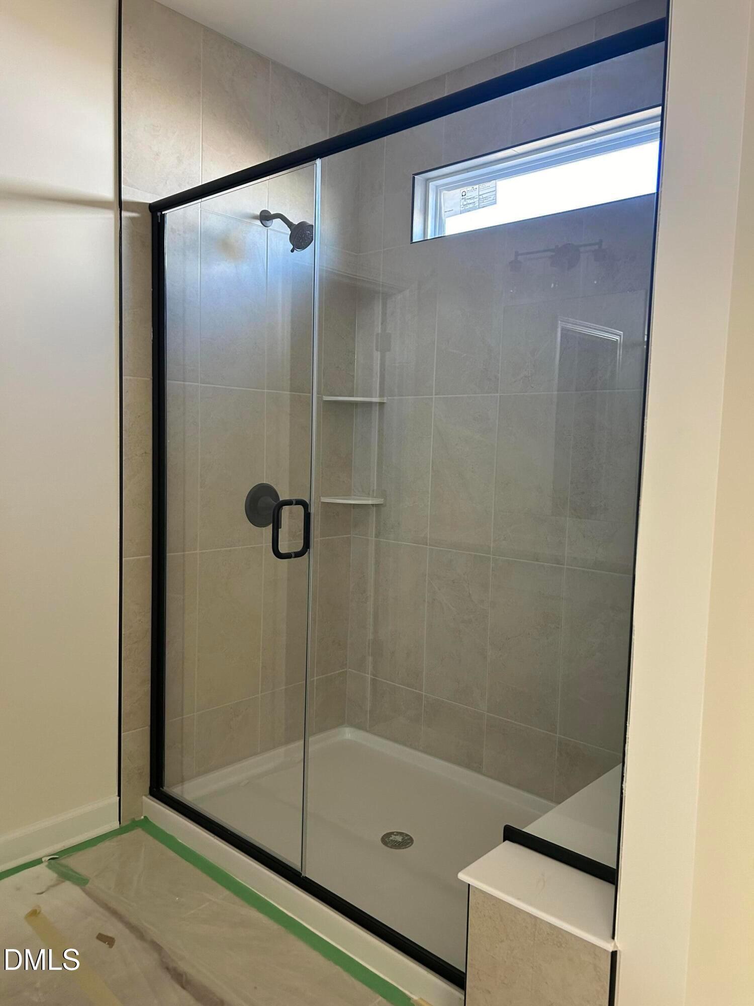 Frameless glass walk-in shower with beige tile walls, built-in bench, and window in master bath of The Magnolia B, Angier, NC