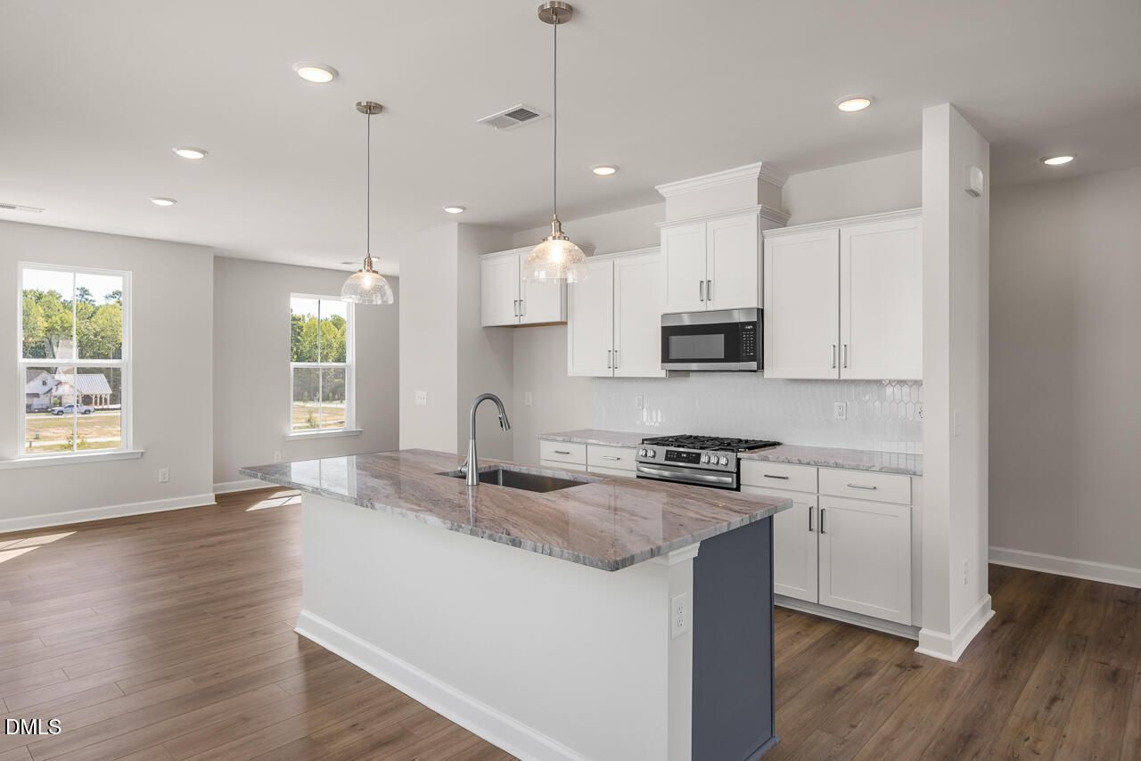 Open-concept kitchen with white cabinetry, granite island, stainless gas range, and hardwood floors in The Mitchell plan, Knightdale NC