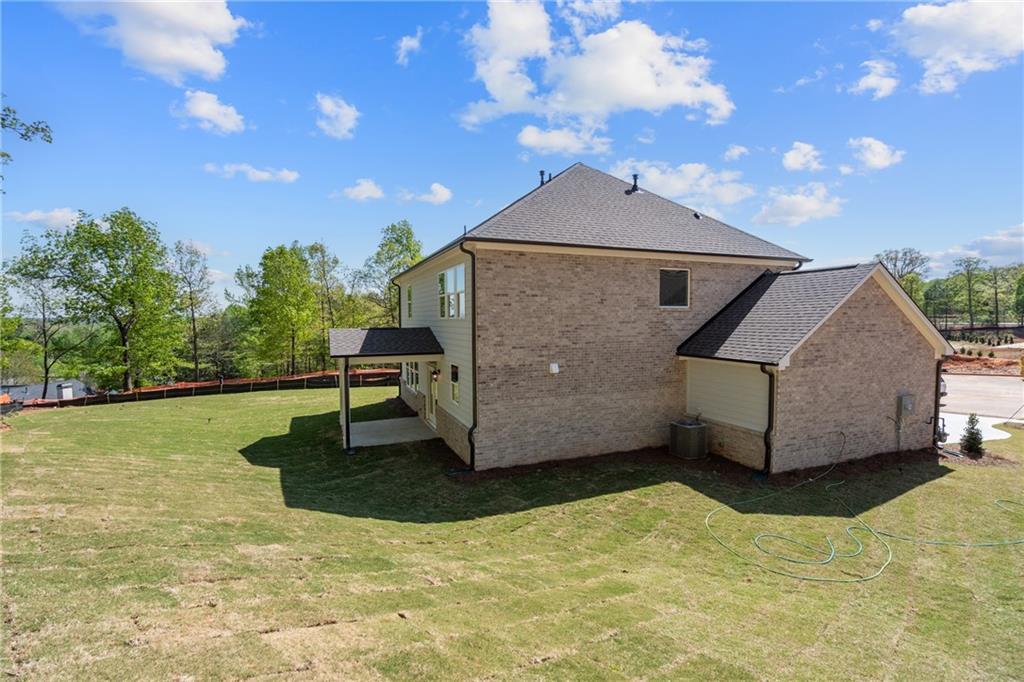 Two-story brick home side view with 3-car garage, covered patio, and lush green yard in Melody Lakeside Estates, Buford, Georgia