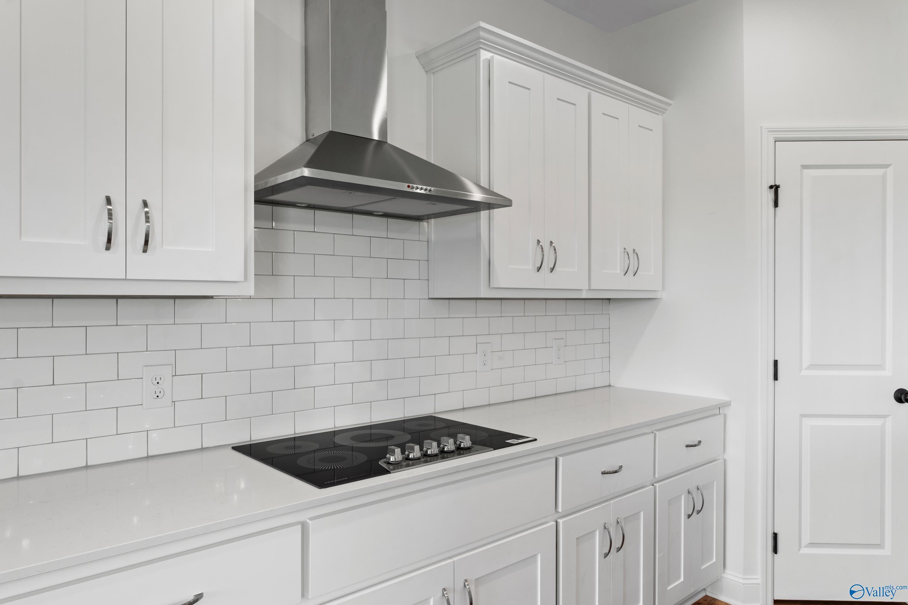Modern white kitchen featuring stainless steel hood, gas cooktop, subway tile backsplash in Davidson Homes The Rockford B, Toney, Alabama