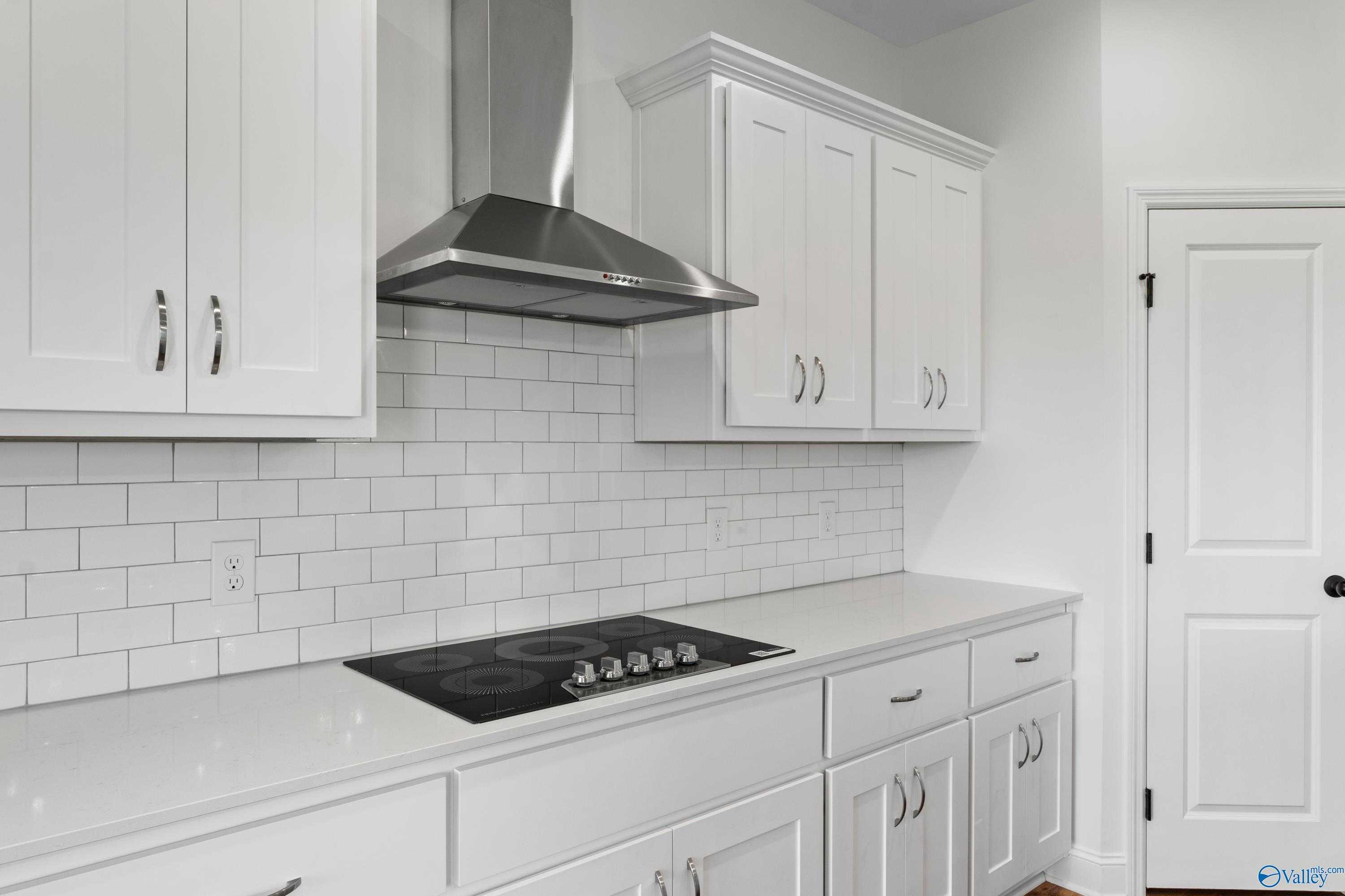 Modern white shaker kitchen with stainless range hood, induction cooktop, subway tile backsplash in Davidson Homes The Rockford B, Toney, AL