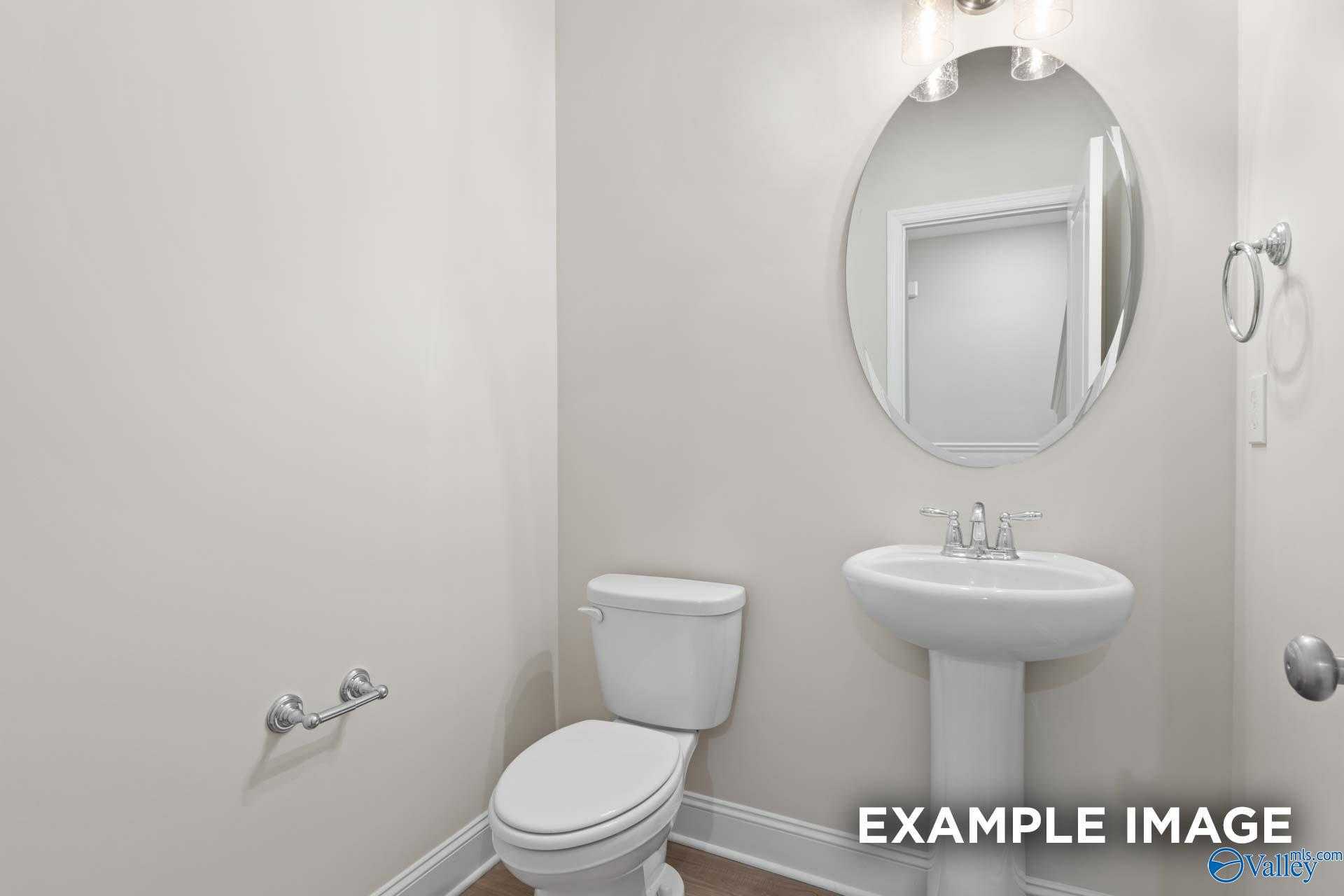 Elegant powder room with pedestal sink, round mirror, and toilet in Davidson Homes The Camden C, Pavilion, Huntsville, Alabama