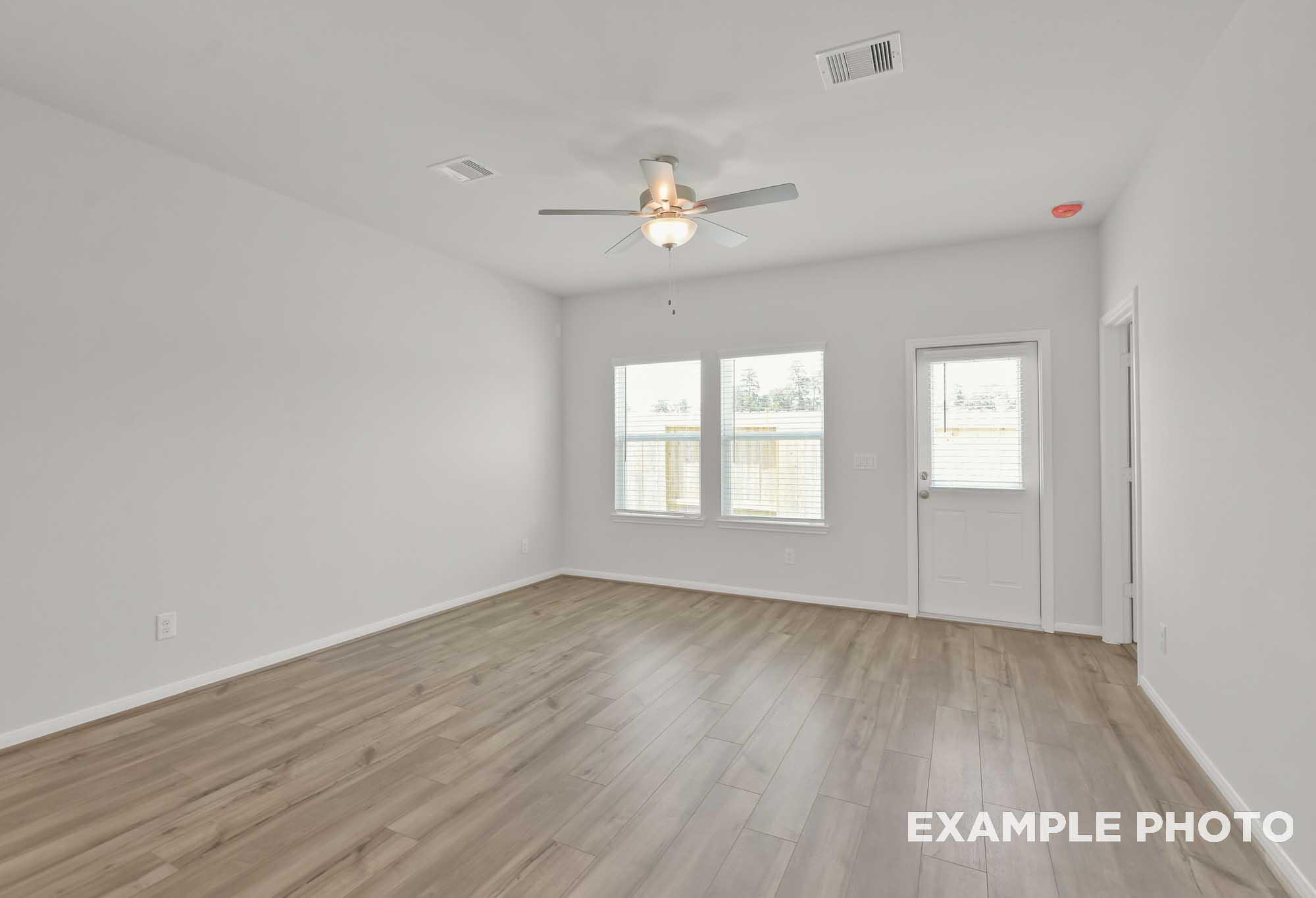 Spacious empty bedroom in The Comal floor plan with light wood laminate floors, white walls, ceiling fan, and large dual windows