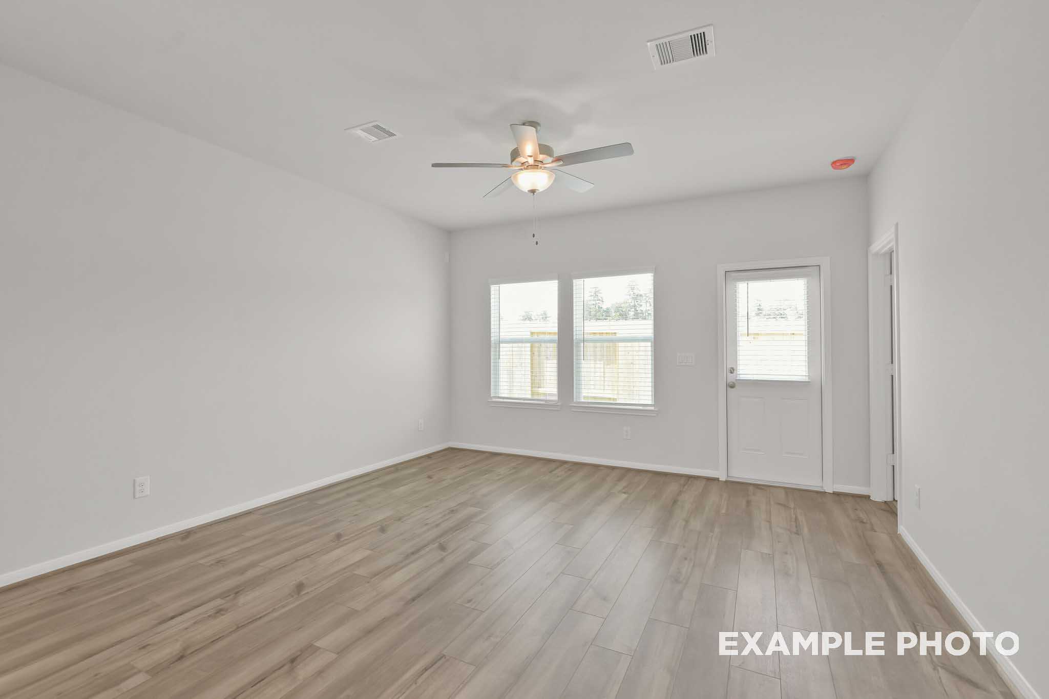 Spacious empty bedroom in The Comal floor plan with light wood laminate floors, white walls, ceiling fan, and large dual windows
