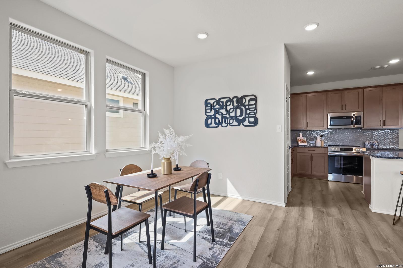 Open dining area with wooden table, black chairs, and rug beside modern kitchen with dark cabinets and stainless appliances in The Daphne H, Seguin, TX