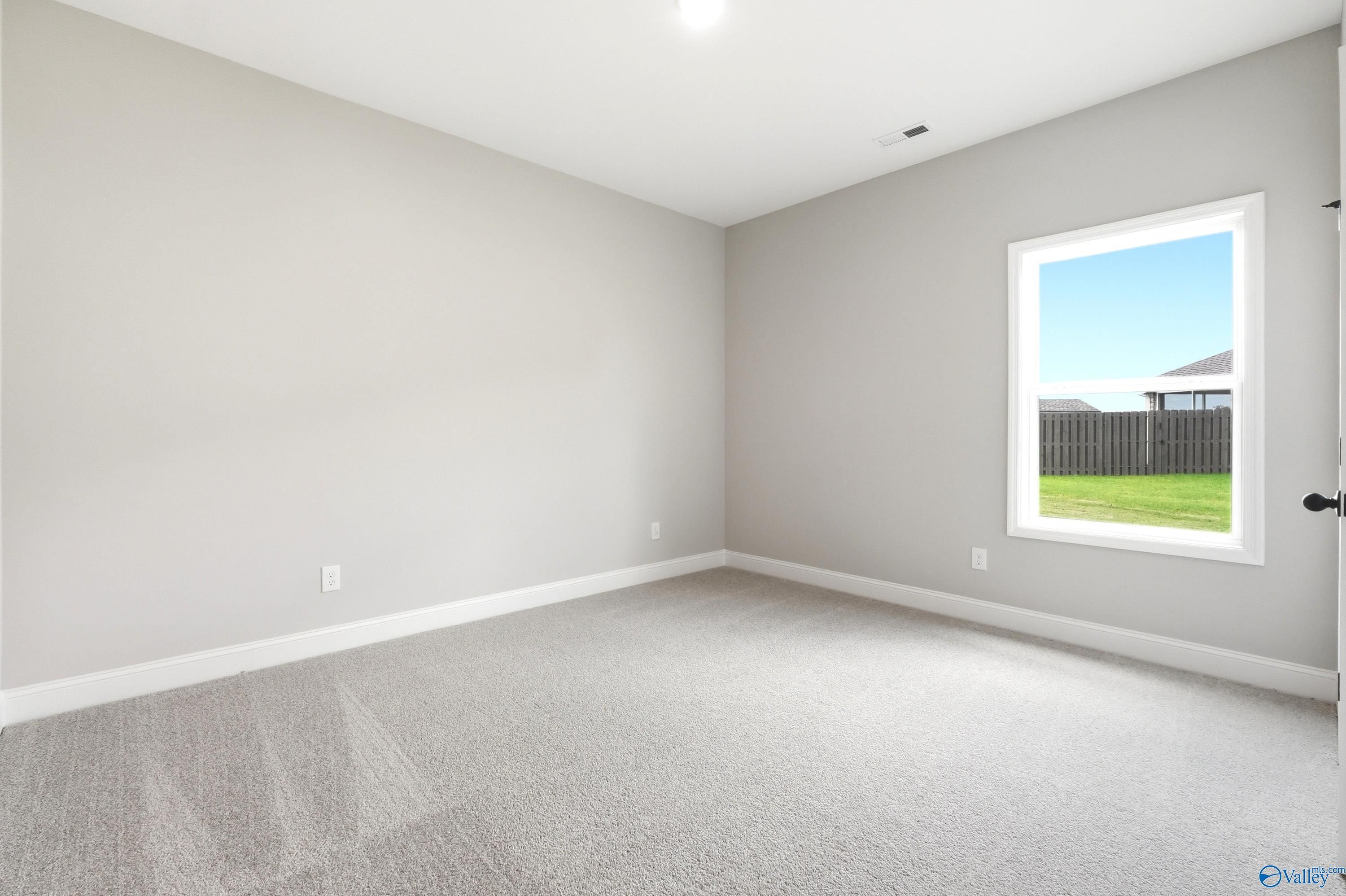 Bright, carpeted bedroom with neutral walls in The Daphne D floor plan at Creekside, Harvest, Alabama.