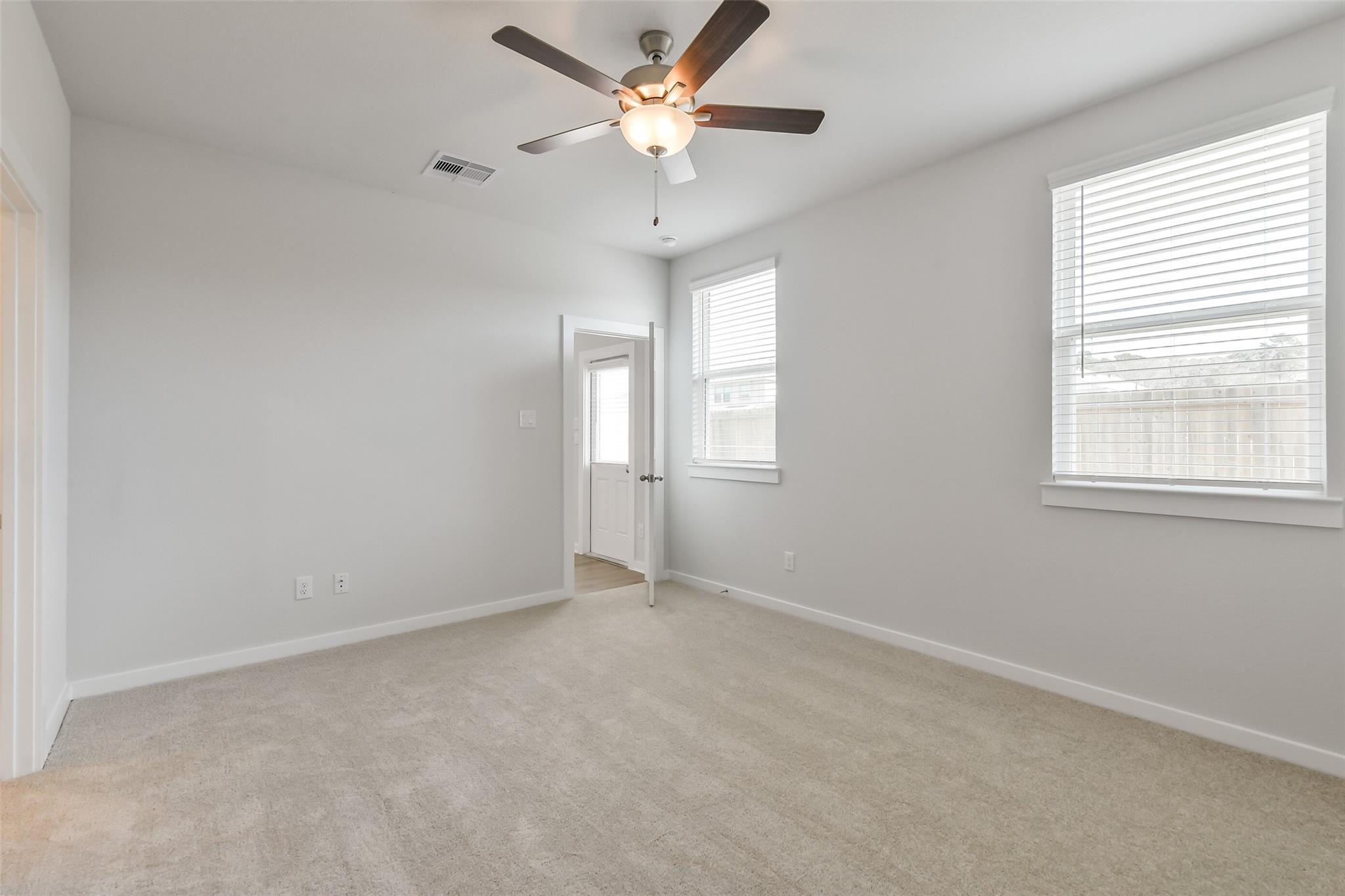 Bright secondary bedroom with ceiling fan, light gray walls, beige carpet, and open door in Davidson Homes The Colorado F, Cleveland, Texas
