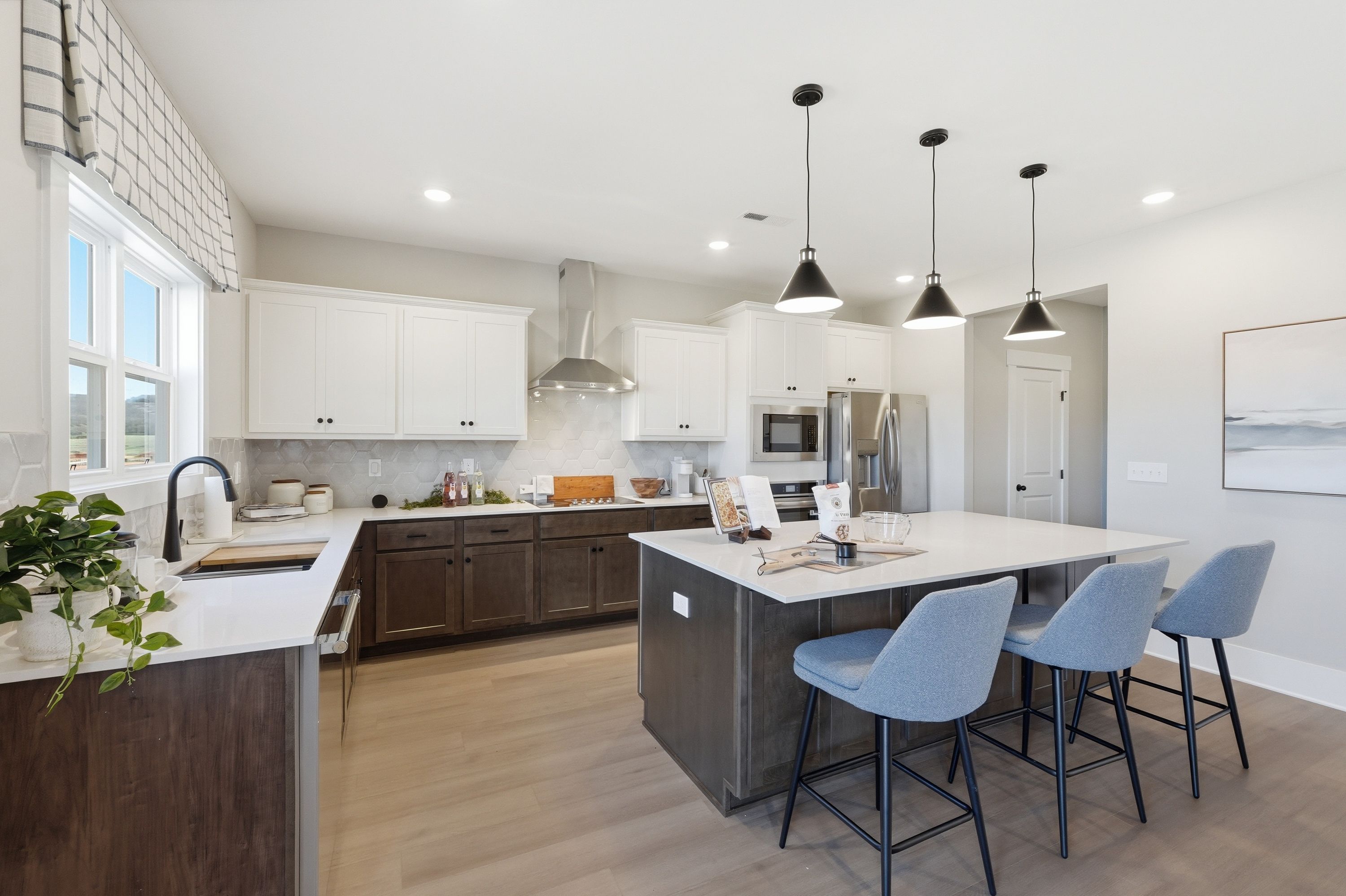 Modern kitchen at Berry Cove in New Market, AL with white cabinets, dark island, quartz counters, blue bar stools, and pendant lights