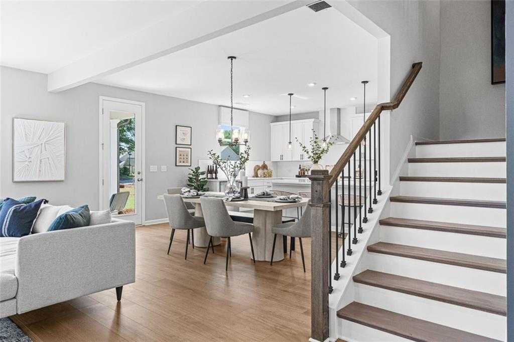 Open-concept living and dining area with modern table, gray sofa, white staircase, and kitchen view in Davidson Homes The Hickory B, Hoschton, GA