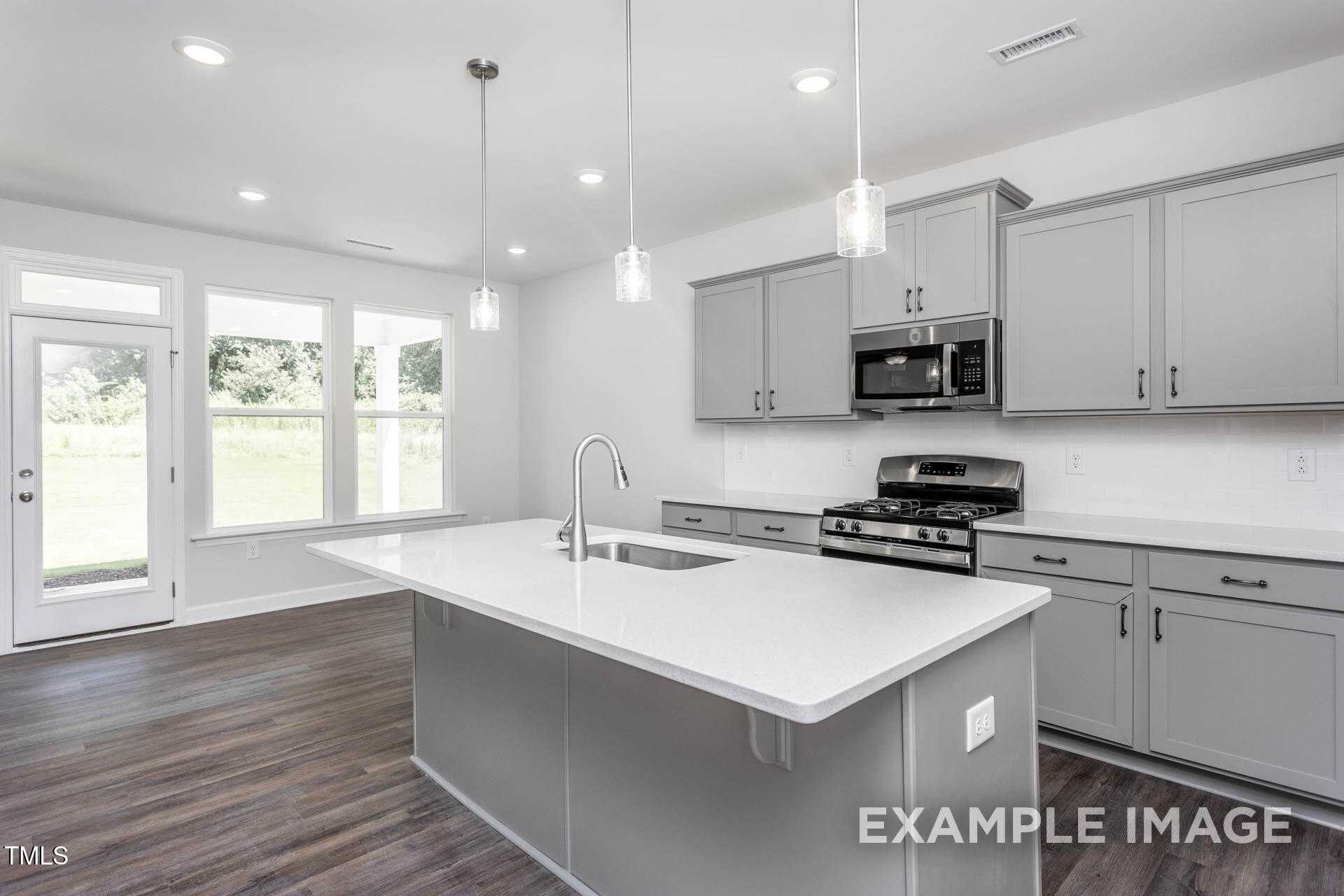 Modern kitchen with gray shaker cabinets, white quartz island, stainless appliances, and large windows in The Willow B floor plan, Lillington, NC