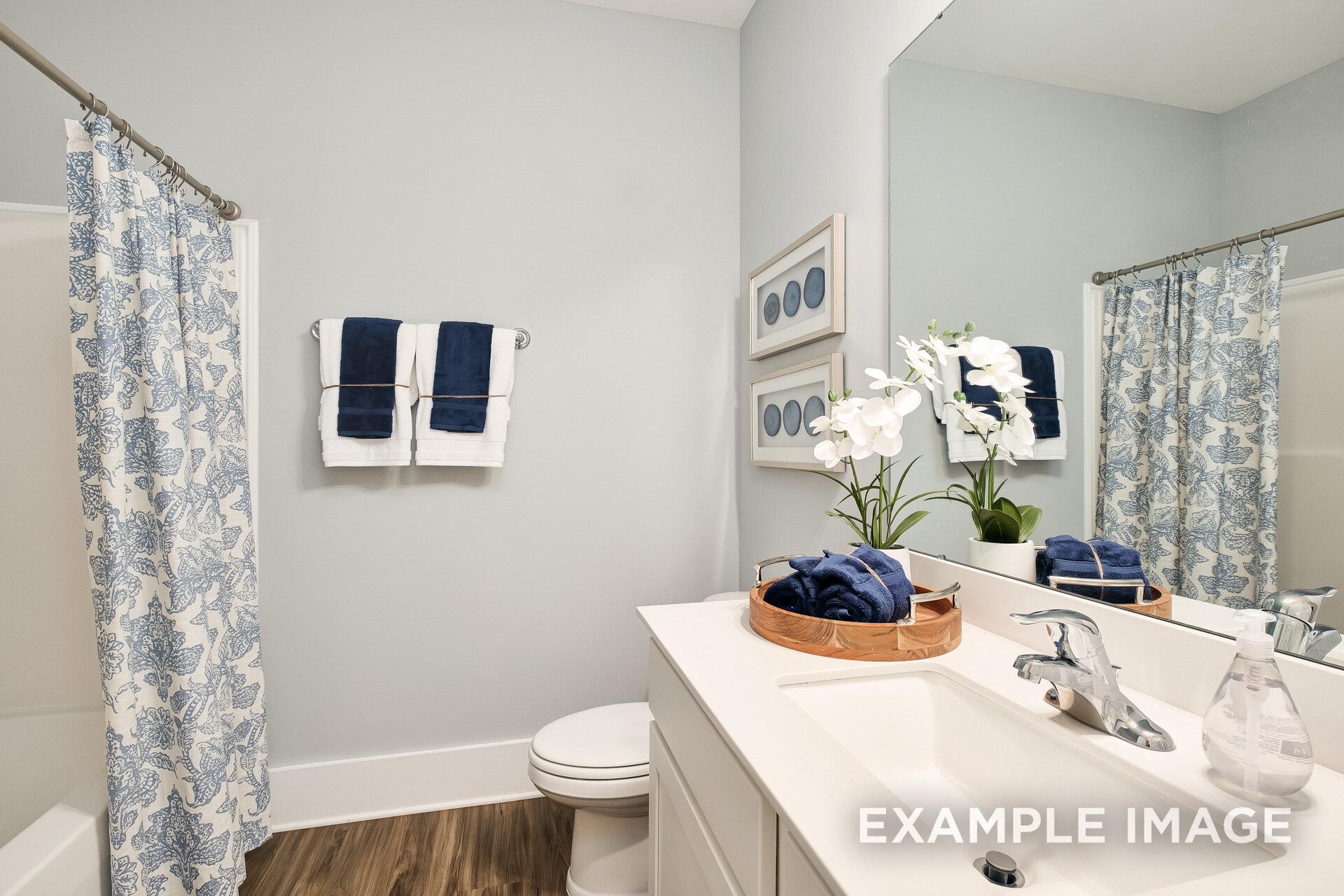 Spacious master bathroom in The Daphne D with gray walls, white vanity, blue floral shower curtain, orchids, and towels